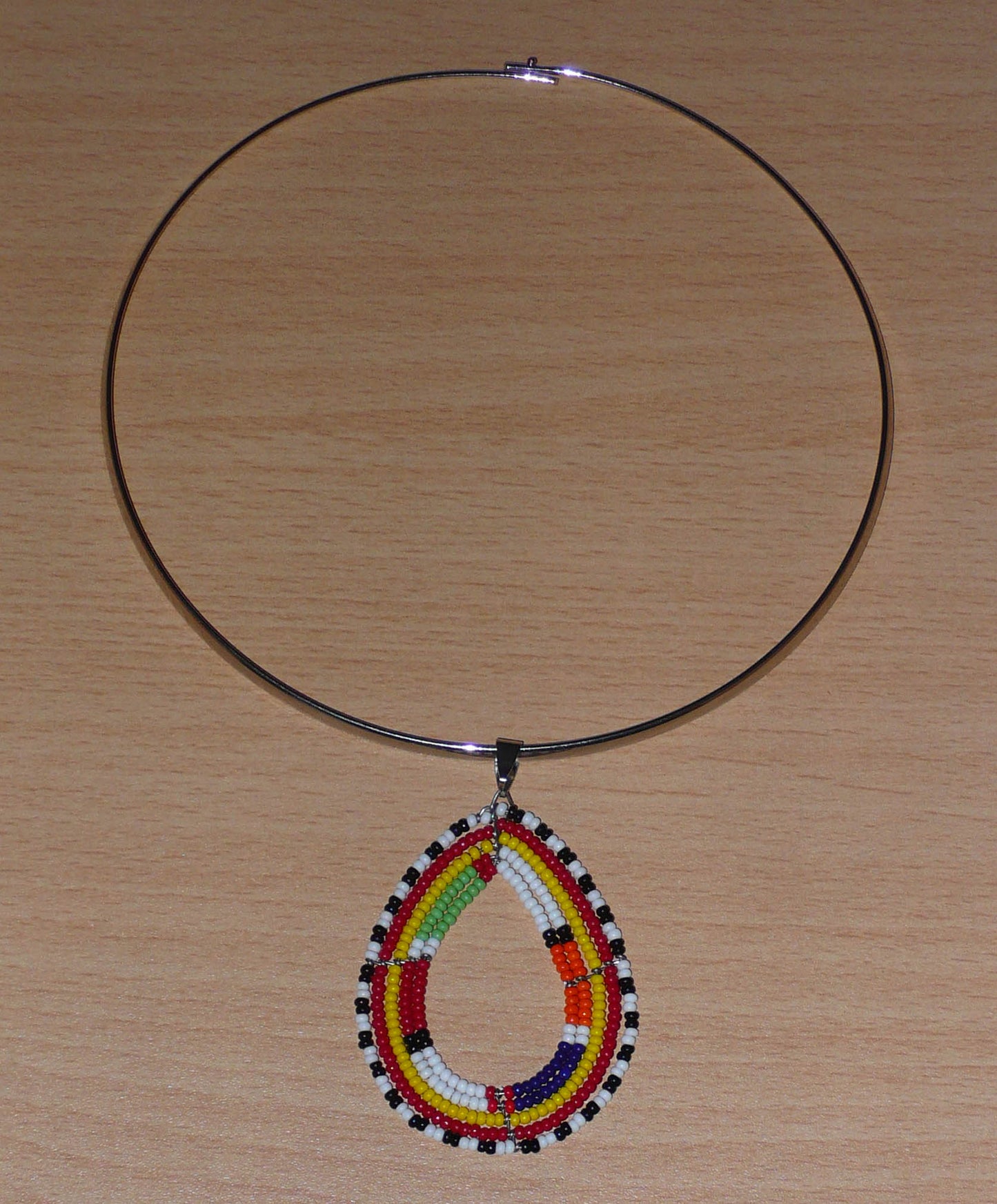 Alliance de tradition Massai et de modernité, ce collier ethnique chic se compose d'un ras de cou en laiton orné d'un pendentif en forme de goutte fait de perles de rocaille multicolores.