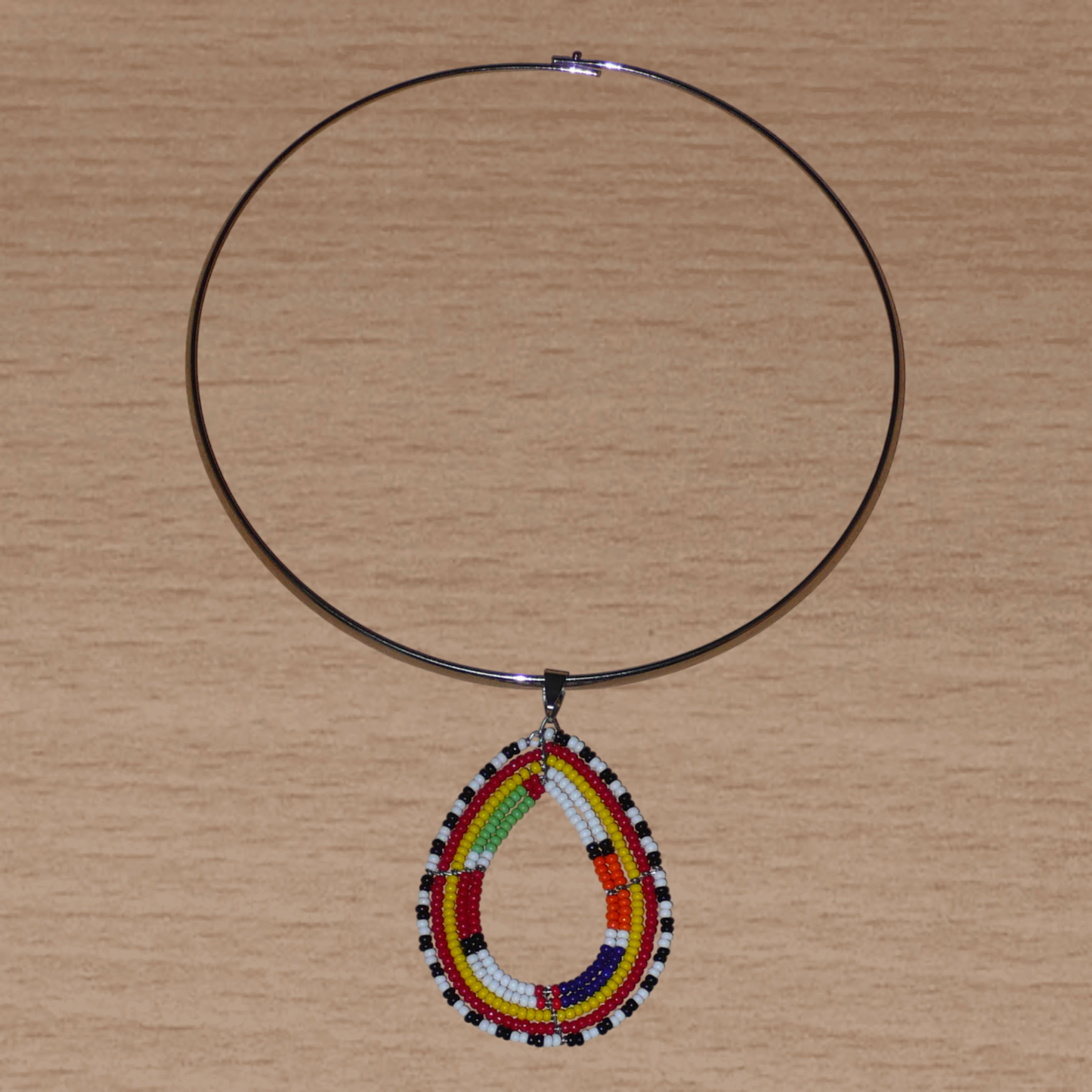 Alliance de tradition Massai et de modernité, ce collier ethnique chic se compose d'un ras de cou en laiton orné d'un pendentif en forme de goutte fait de perles de rocaille multicolores.