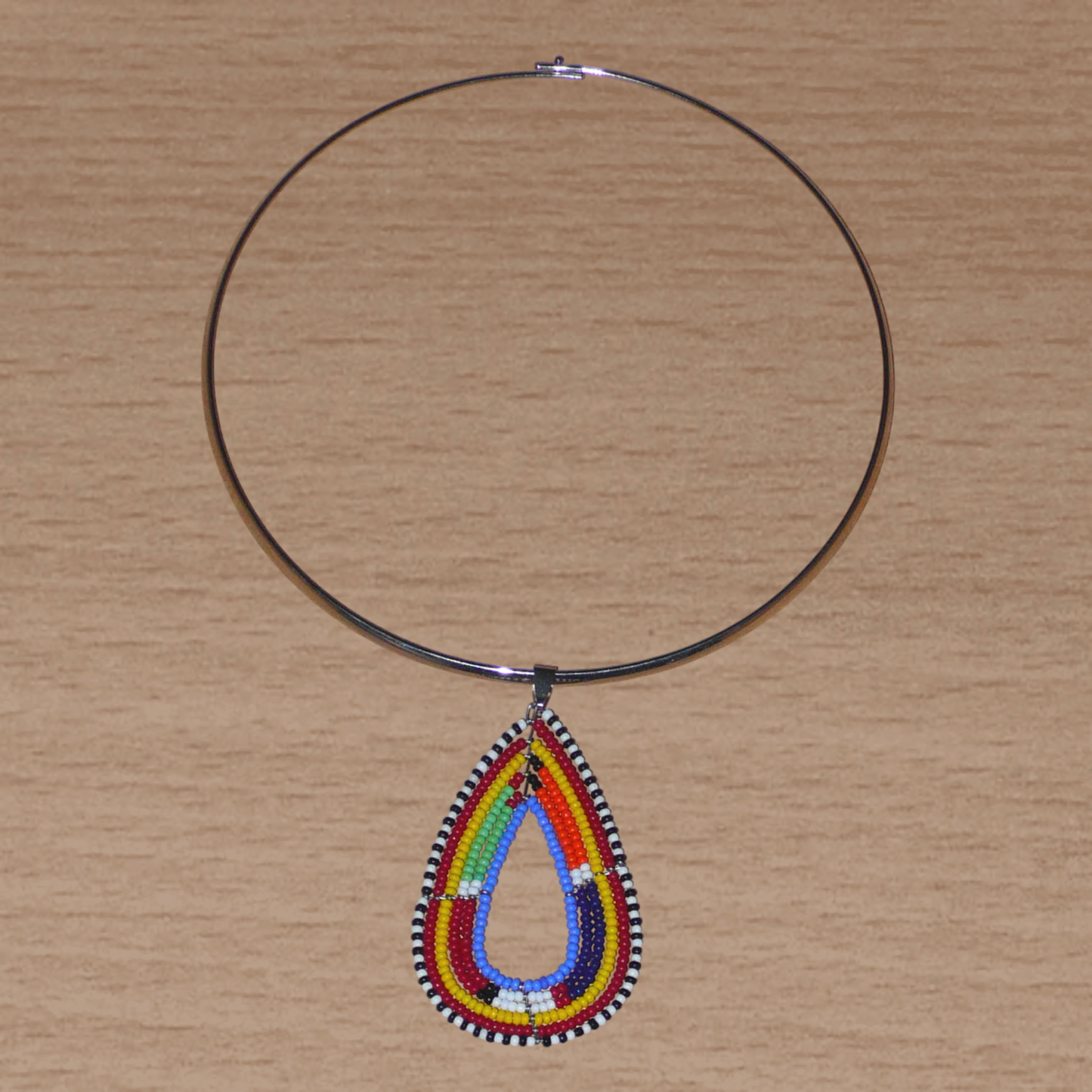 Collier africain composé d'un ras de cou en laiton rehaussé d'un pendentif aux couleurs et motifs Massai fait de perles de rocaille bleues et multicolores montées en goutte.