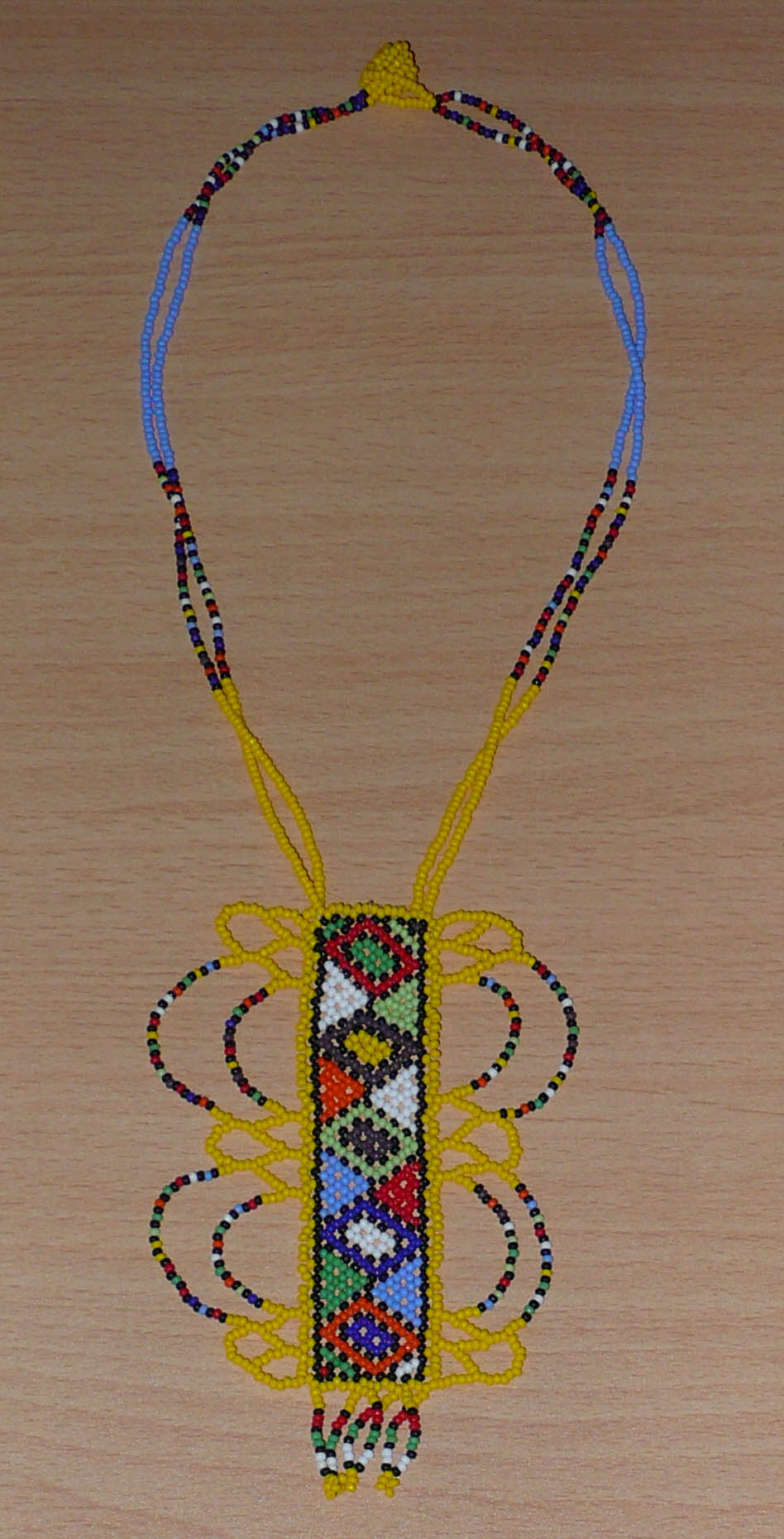 Collier africain jaune orné d'un long pendentif décoré de motifs ethniques zoulous multicolores composé de perles de rocaille.