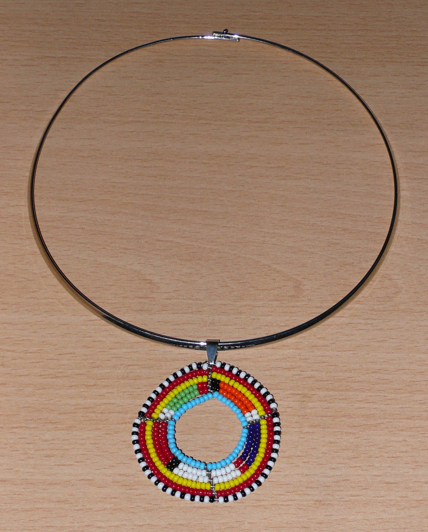 Collier africain ethnique composé d'un ras de cou en laiton agrémenté d'un médaillon traditionnel Massai fait de perles de rocaille multicolores.