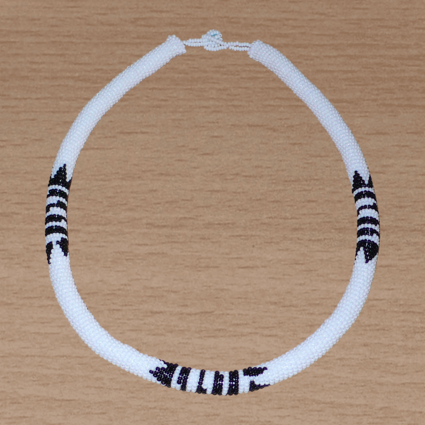 Collier africain zoulou blanc à motifs ethniques traditionnels noirs composé perles de rocaille tissées et enroulées autour d'un tube.