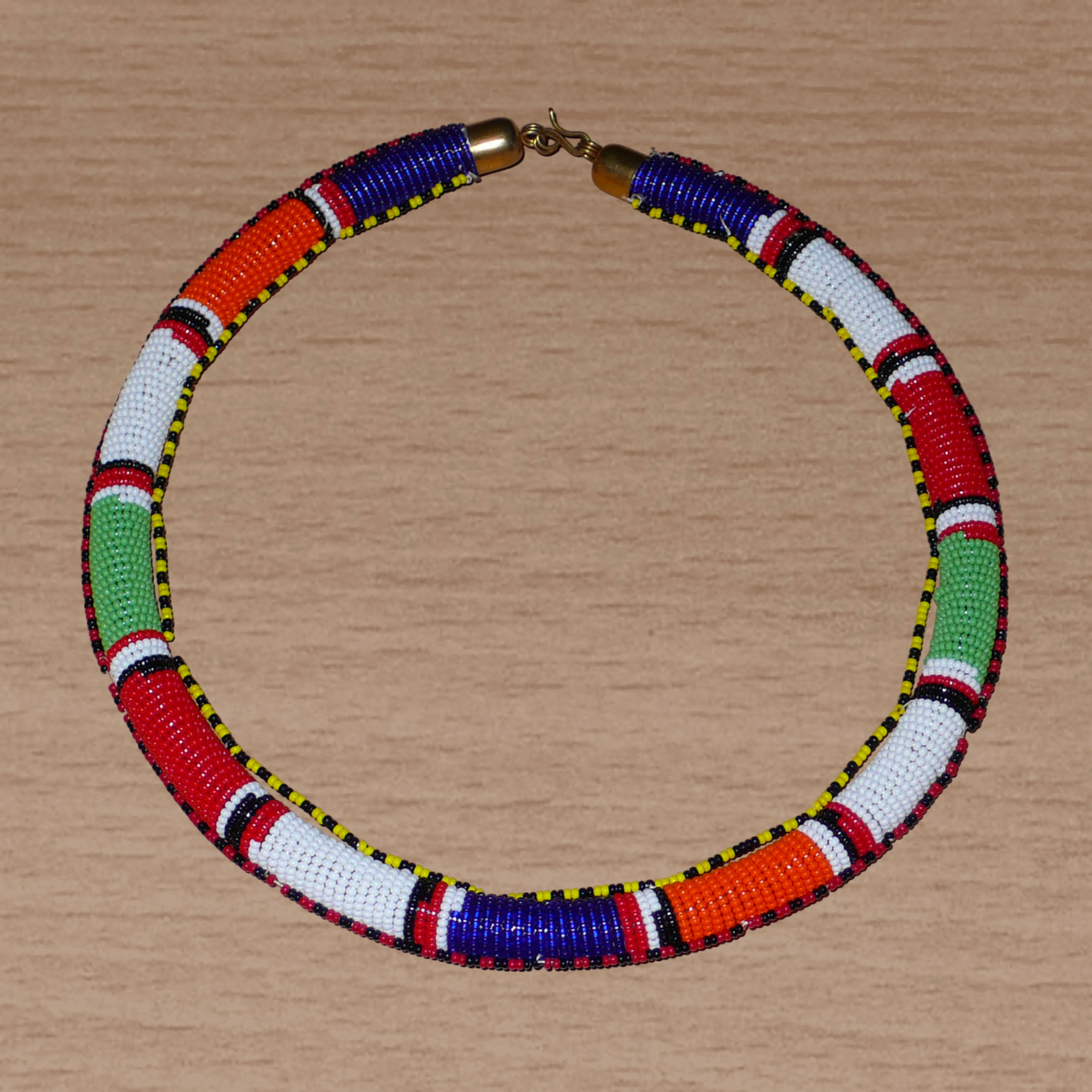 Collier africain tribal à motifs traditionnels Massai composé de perles de rocaille principalement rouges, vertes, blanches, bleu foncé et orange tissées et enroulées autour d'un tube.