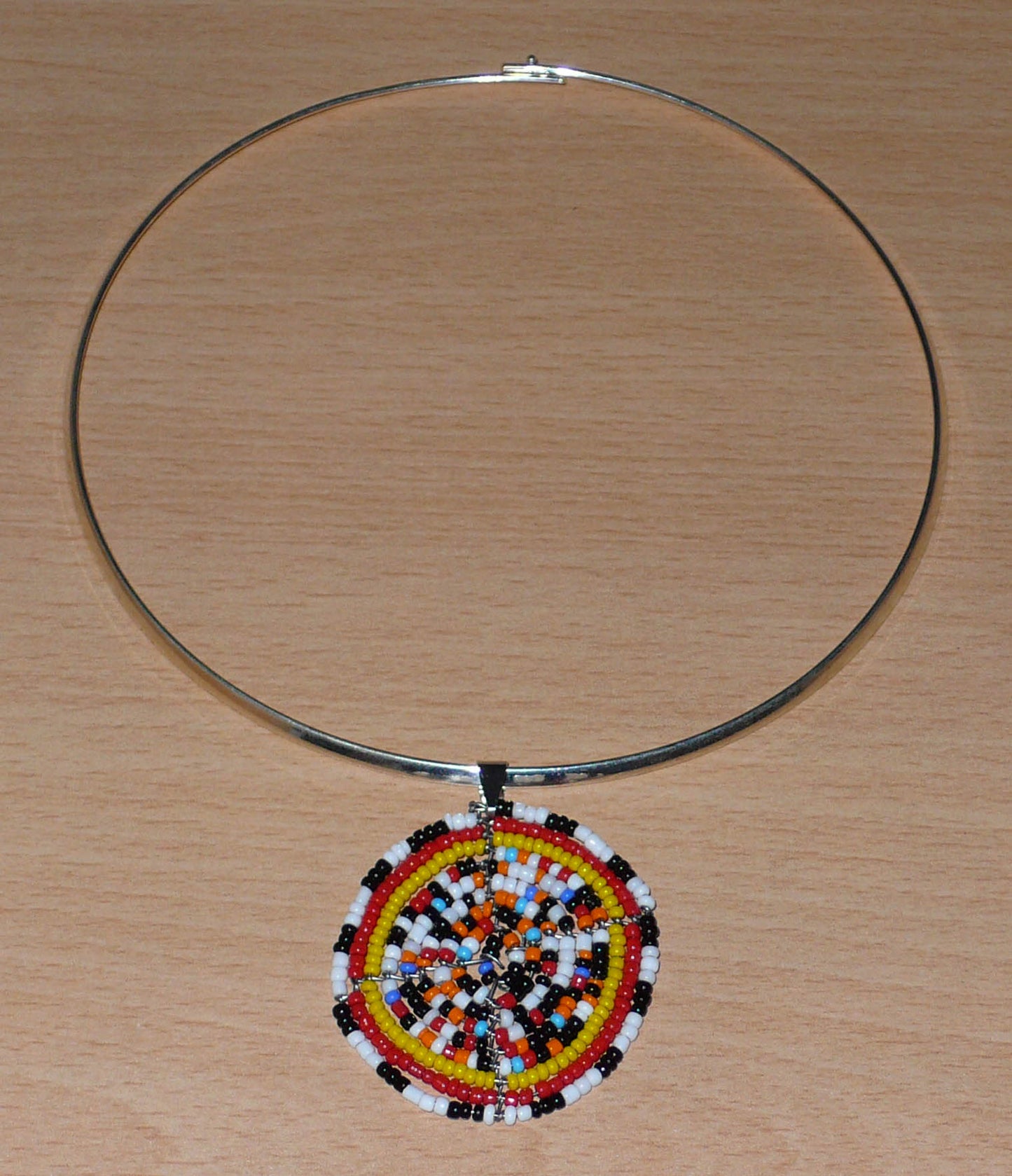 Collier ras de cou ethnique en laiton orné d'un médaillon fait d'un mélange de perles de rocaille multicolore. Il mesure 19 cm de long, le ras de cou en laiton a une circonférence de 42,5 cm avec un diamètre de 13,5 cm ; le médaillon mesure 5 cm de long et de large.
