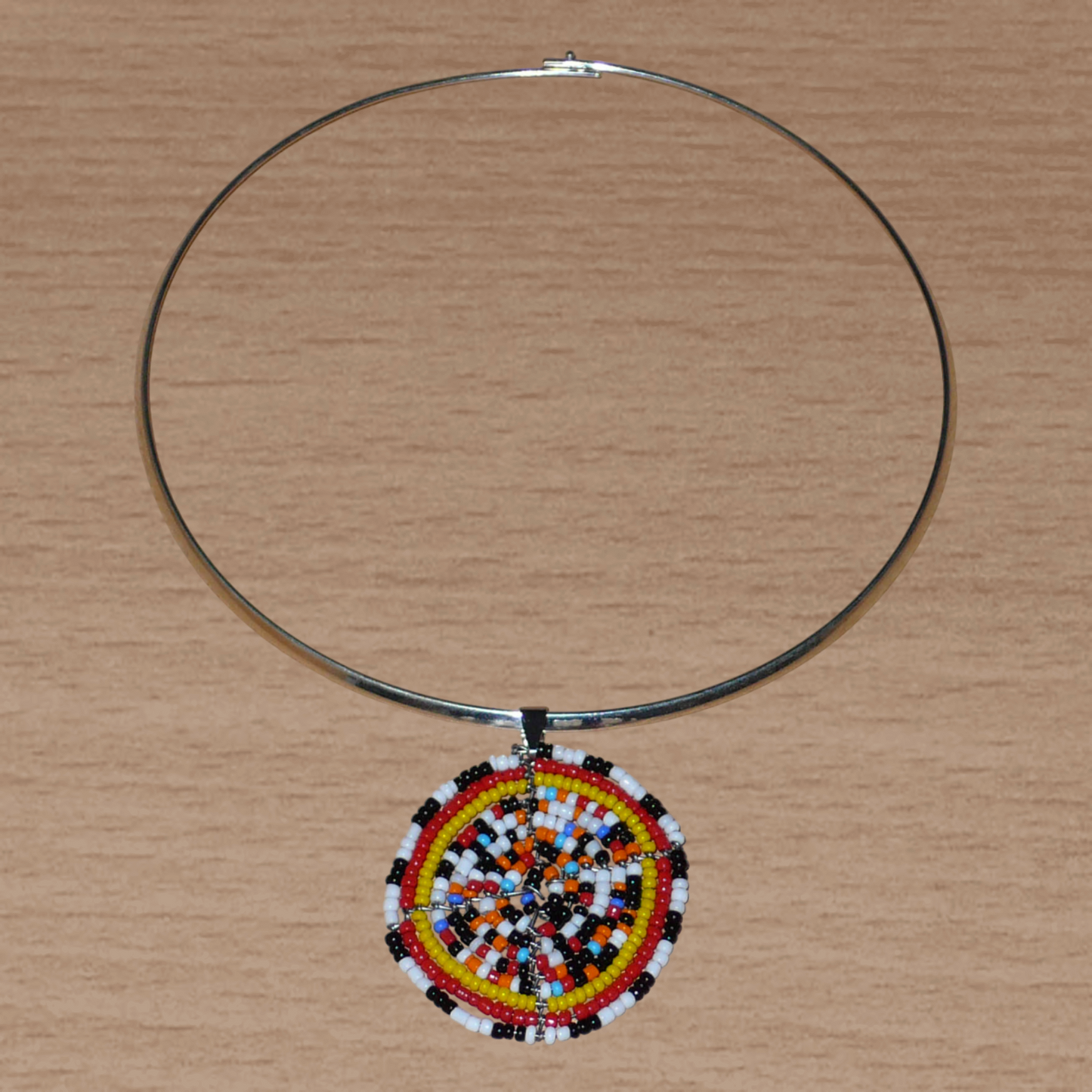Collier ras de cou ethnique en laiton orné d'un médaillon fait d'un mélange de perles de rocaille multicolore. Il mesure 19 cm de long, le ras de cou en laiton a une circonférence de 42,5 cm avec un diamètre de 13,5 cm ; le médaillon mesure 5 cm de long et de large.