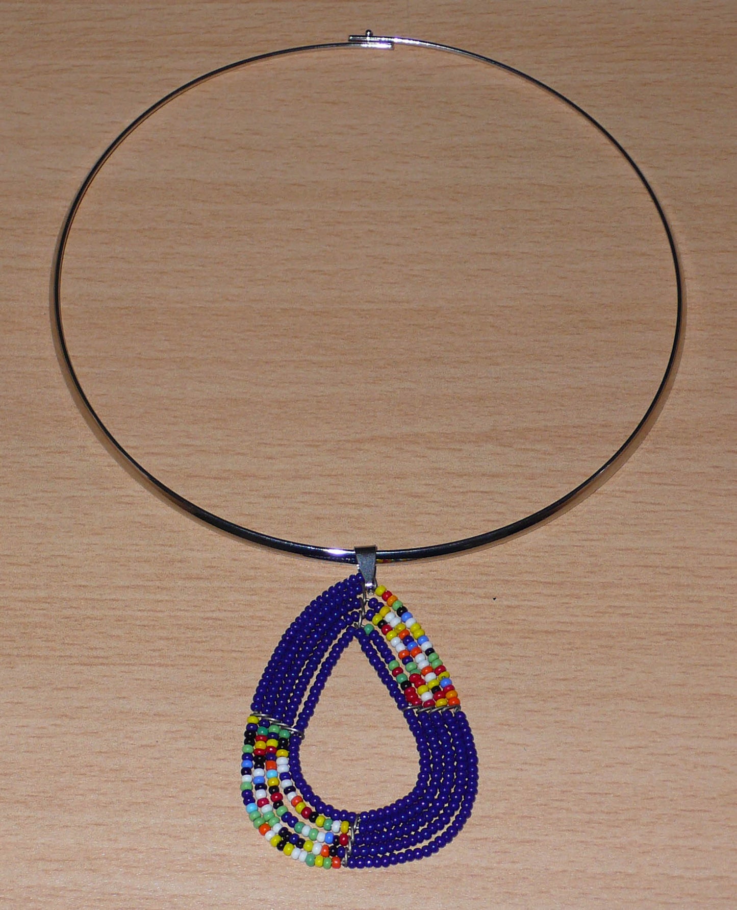 Collier ethnique composé d'un ras de cou en laiton agrémenté d'un pendentif de forme triangulaire aux angles arrondis fait de perles de rocaille bleu marine et multicolores.