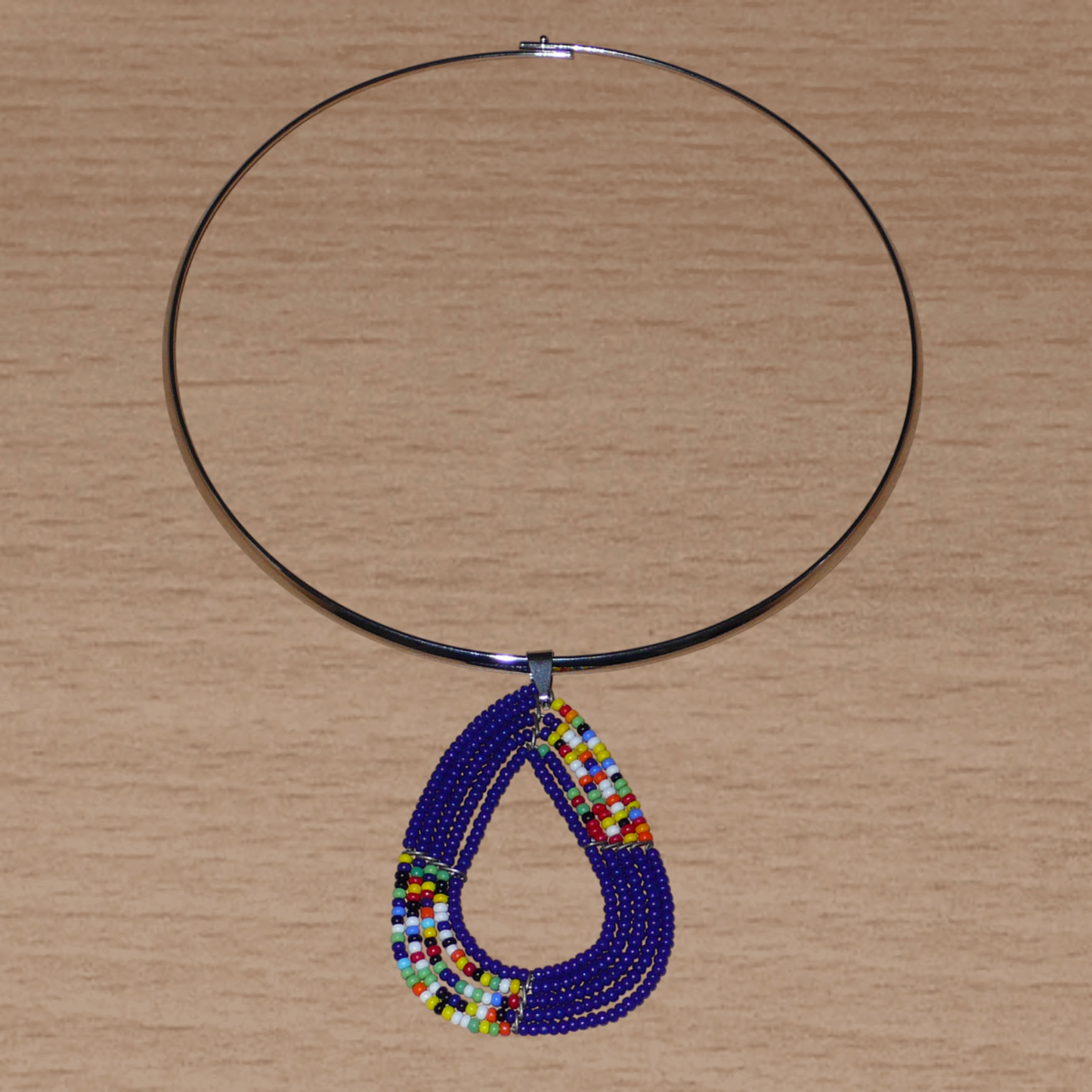 Collier ethnique composé d'un ras de cou en laiton agrémenté d'un pendentif de forme triangulaire aux angles arrondis fait de perles de rocaille bleu marine et multicolores.