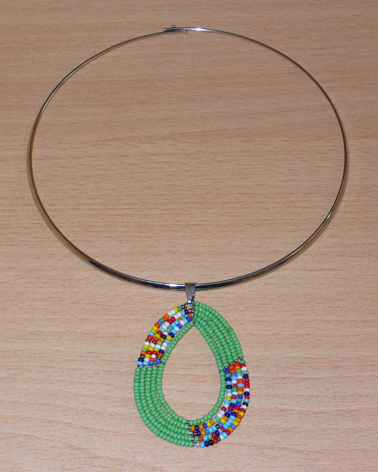 Collier ethnique aux accents bohème composé d'un ras de cou en laiton rehaussé d'un pendentif fait de perles de rocaille vertes et multicolores montées en forme de goutte.