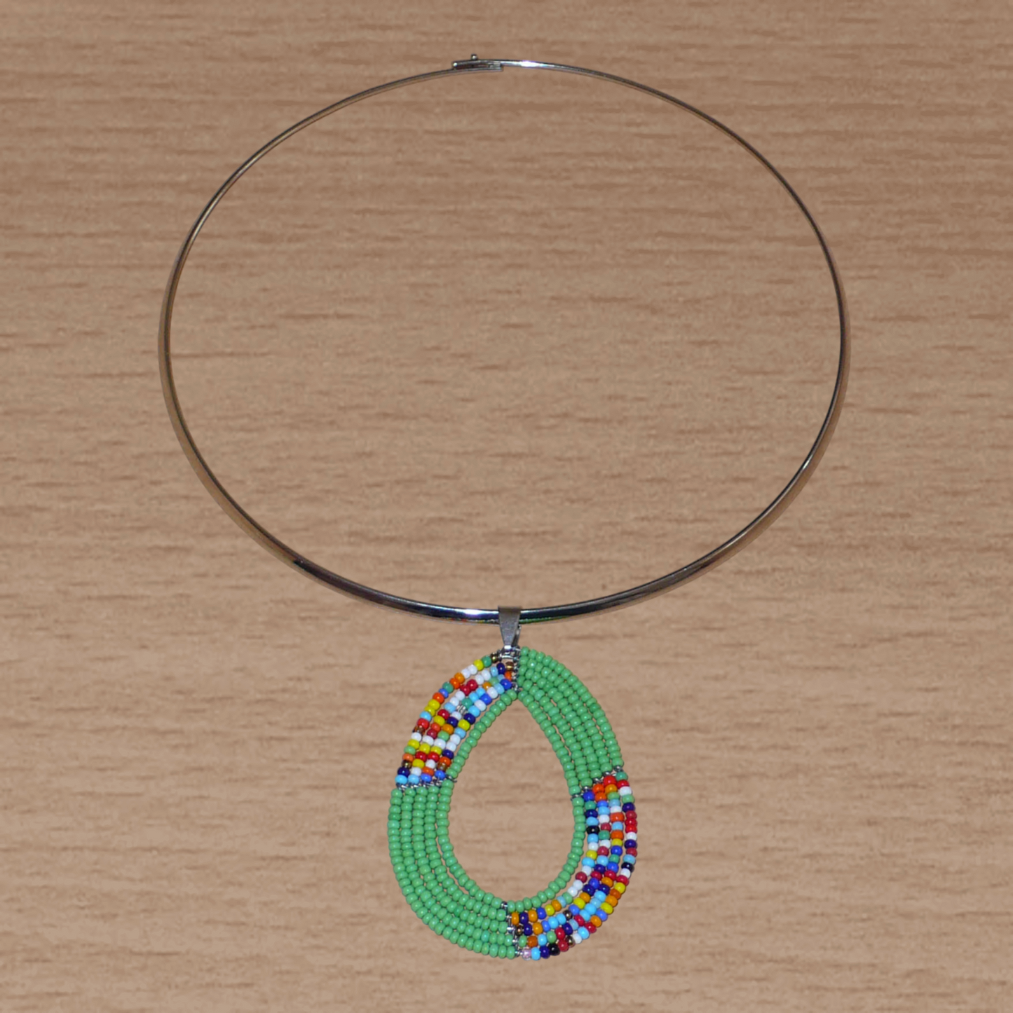 Collier ethnique aux accents bohème composé d'un ras de cou en laiton rehaussé d'un pendentif fait de perles de rocaille vertes et multicolores montées en forme de goutte.