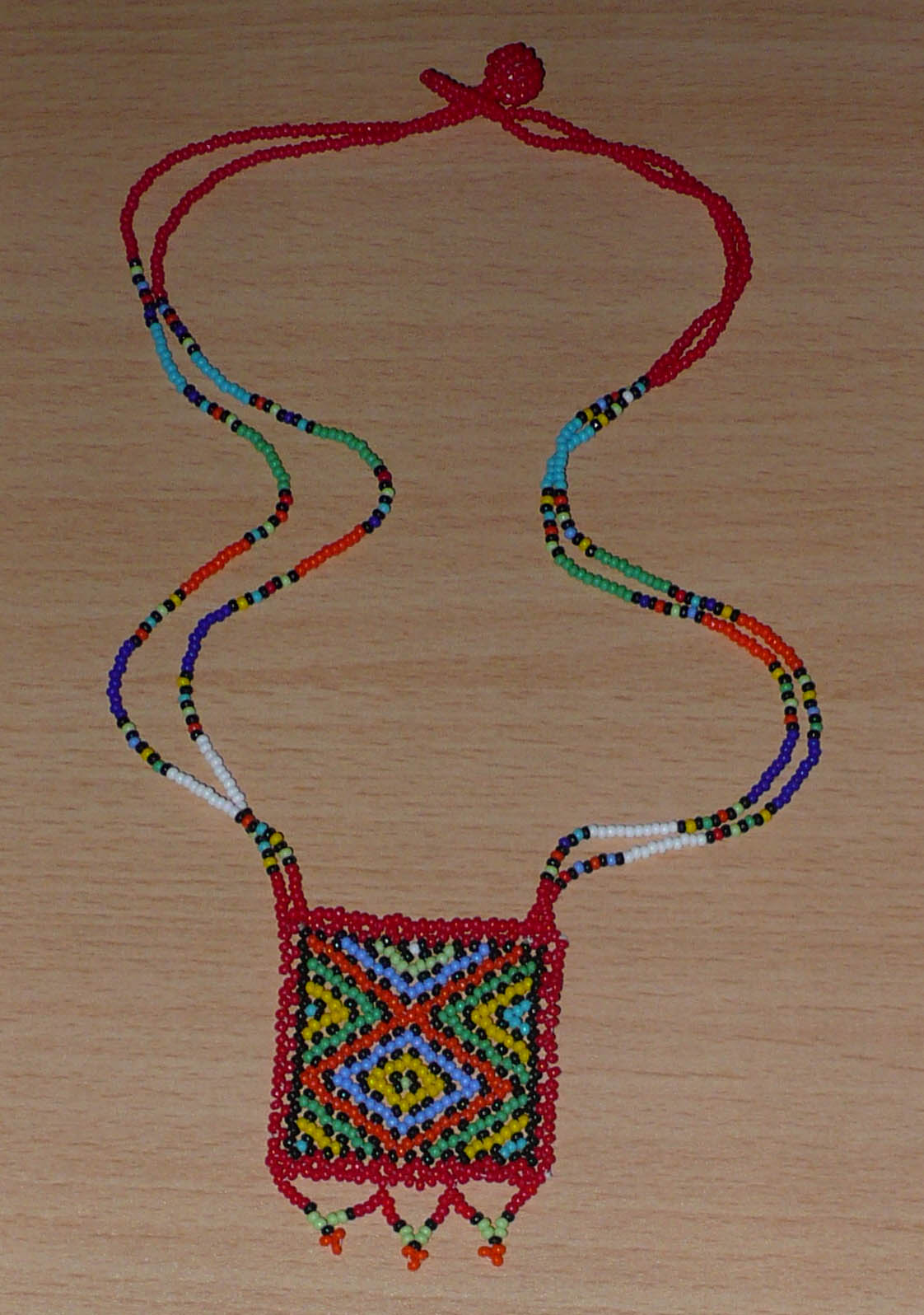 Collier africain "Zulu Love Letter" avec pendentif orné de motifs ethniques ; il se compose d'un tissage de perles de rocaille rouges et multicolores.