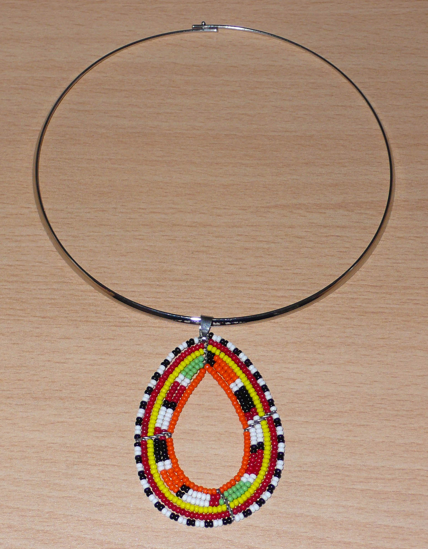 Collier africain composé d'un ras de cou en laiton décoré d'un long et large pendentif en forme de goutte et à motifs ethniques Massai fait de perles de rocaille.