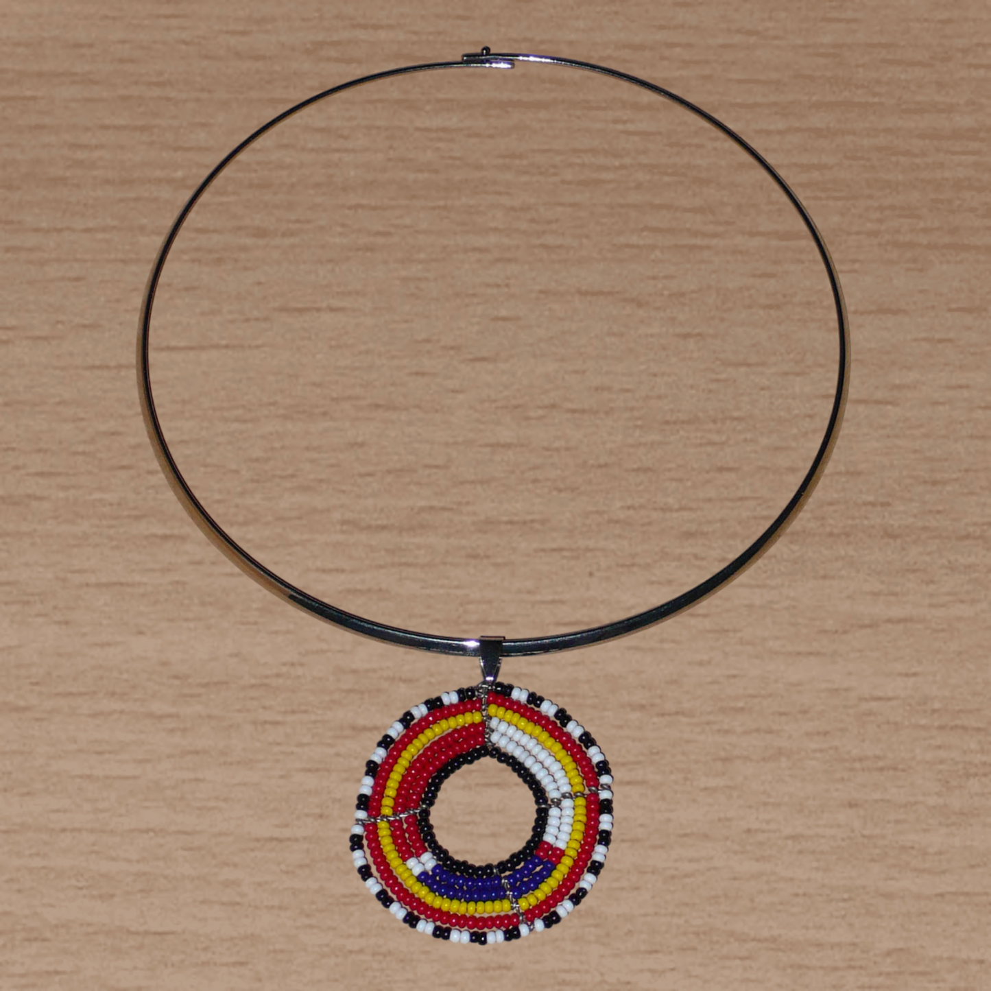 Collier ethnique contemporain se composant d'un ras de cou en laiton orné d'un pendentif rond à motifs Massai fait d'un tissage de perles de rocaille rouges, blanches, bleues, jaunes, noires et blanches.