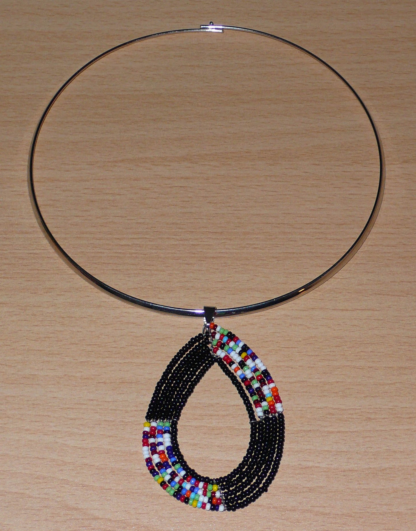 Collier ras de cou en laiton orné d'un long pendentif en forme de goutte composé de perles de rocaille noires et multicolores.