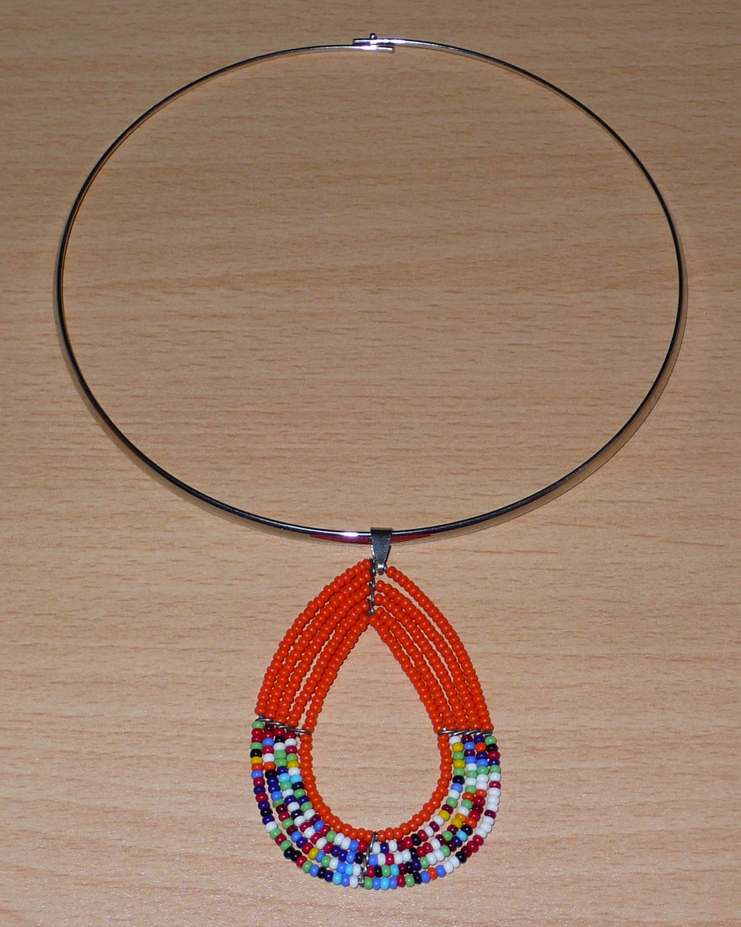 Collier ras de cou en laiton orné d'un long pendentif en forme de goutte composé de perles de rocaille orange et multicolores.