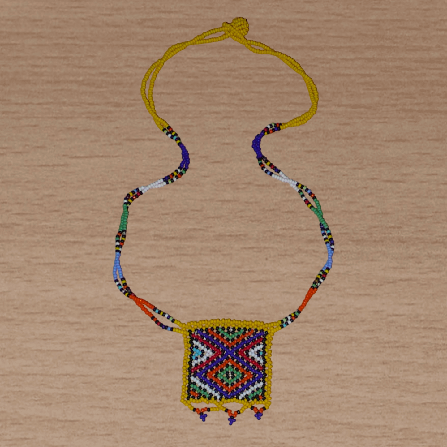Collier africain Zoulou avec pendentif orné de motifs ethniques traditionnels. Il se compose de perles de rocaille jaunes et multicolores et s'attache avec un fermoir à boule.