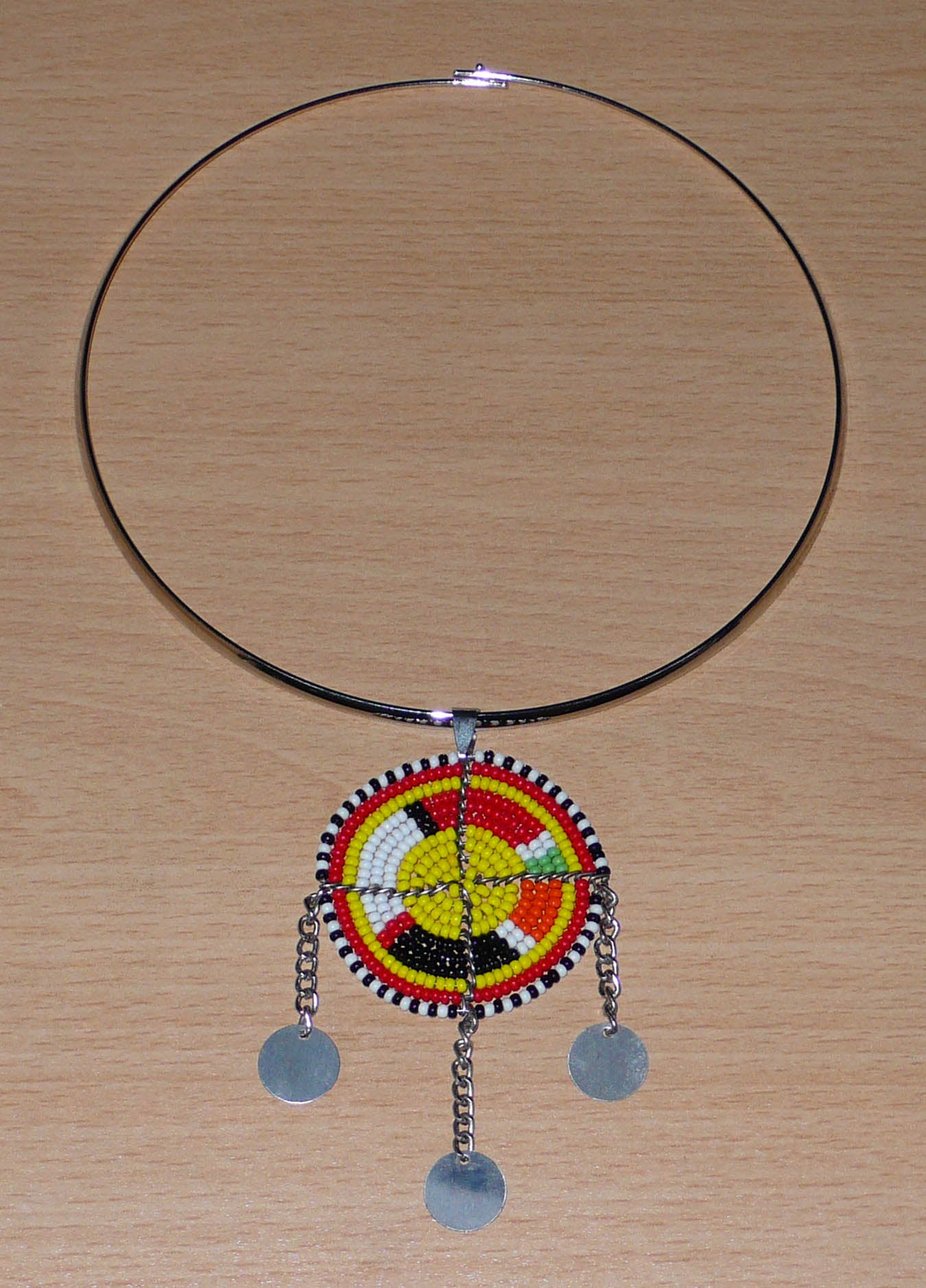 Collier ethnique chic composé d'un ras de cou en laiton rehaussé d'un pendentif Massai fait de perles de rocaille multicolores et de chaînettes décorées de disques métalliques.