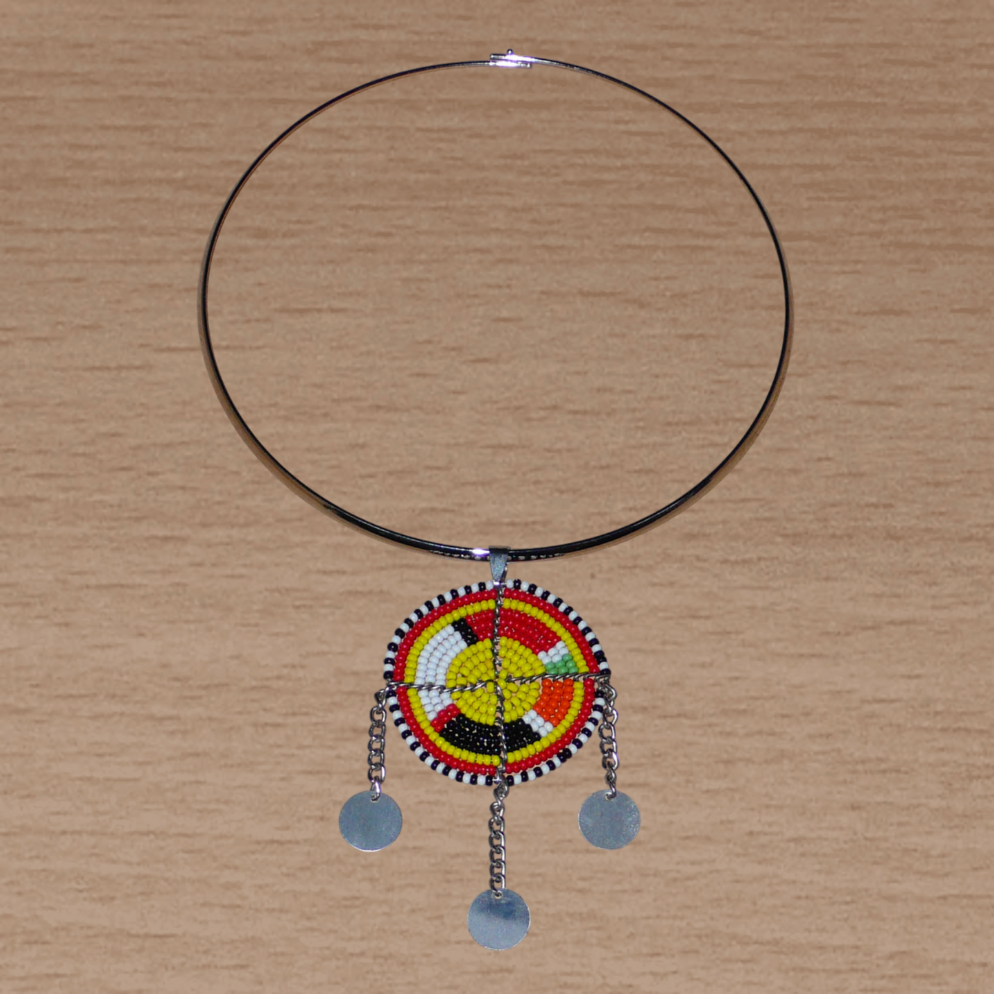 Collier ethnique chic composé d'un ras de cou en laiton rehaussé d'un pendentif Massai fait de perles de rocaille multicolores et de chaînettes décorées de disques métalliques.