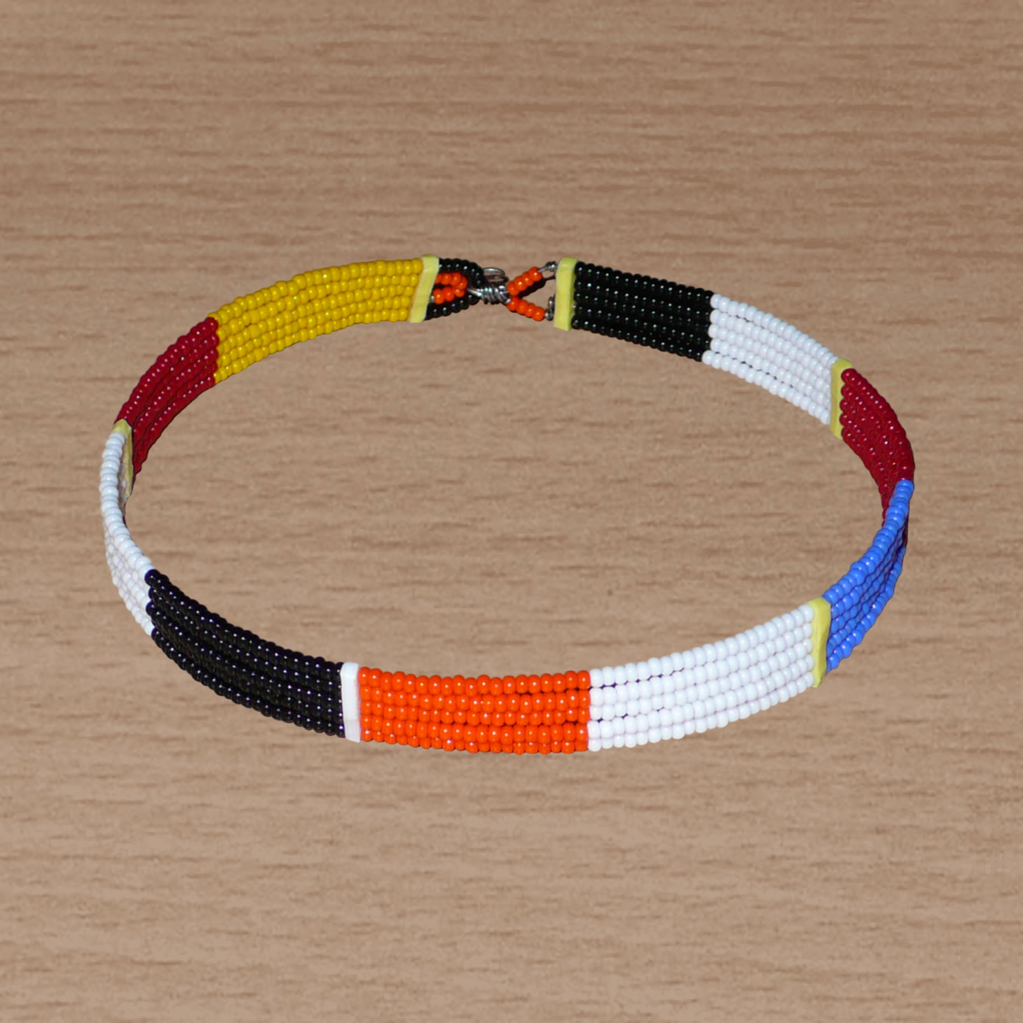 Collier ras de cou africain Massai fait de cinq rangées de perles de rocaille orange, noires, blanches, rouges et jaunes. Sa longueur autour du cou est de 35,5 cm et sa largeur de 1 cm ; il s'attache avec un crochet.