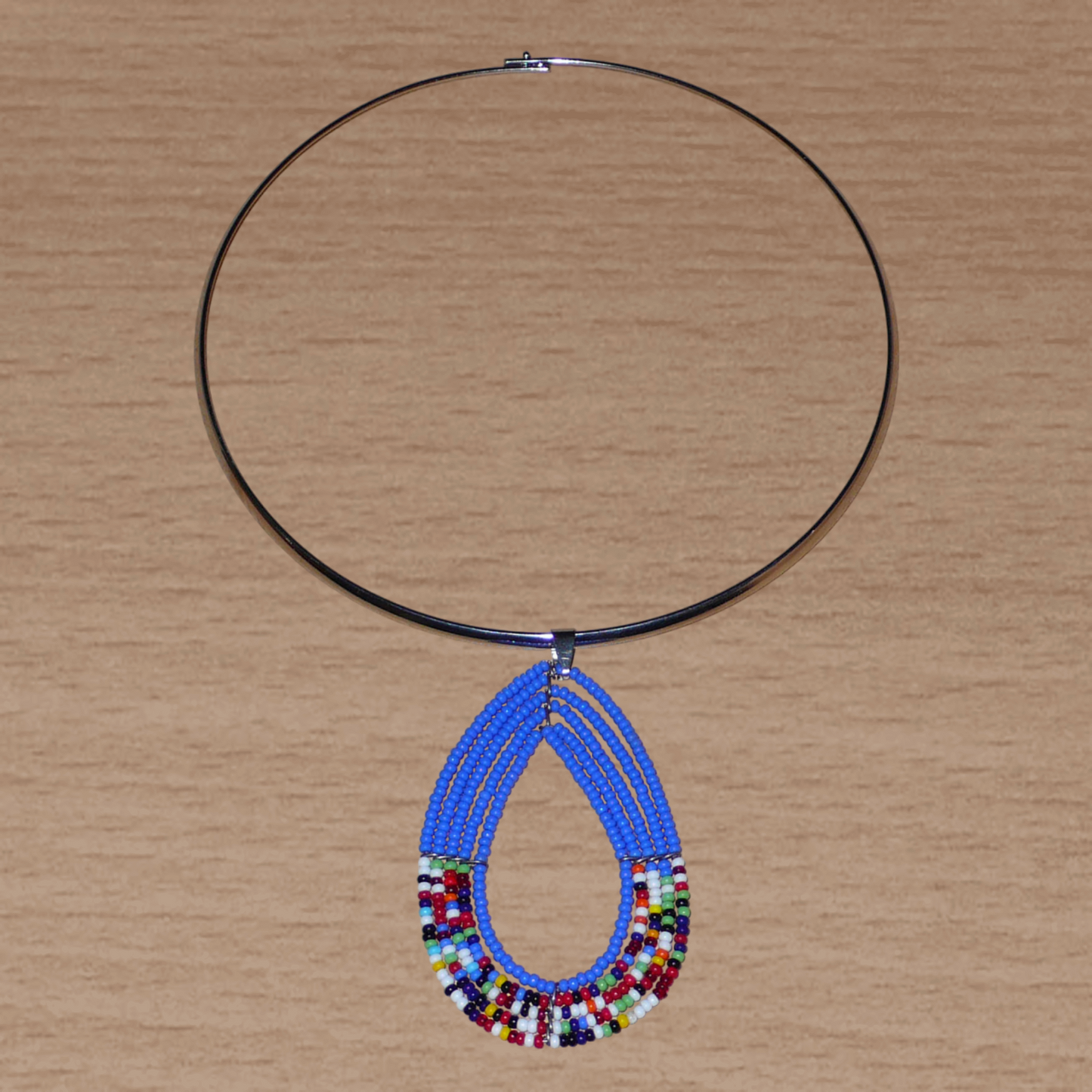 Collier ras de cou bleu et multicolore en laiton orné d'un long pendentif fait de perles de rocaille enfilées sur cinq rangées de fils de fer montés en forme de goutte. Il mesure 21 cm de long, la circonférence du ras de cou est de 4,5 cm avec un diamètre de 13,5 cm ; le pendentif mesure 7 cm de long et 4,5 cm de large.