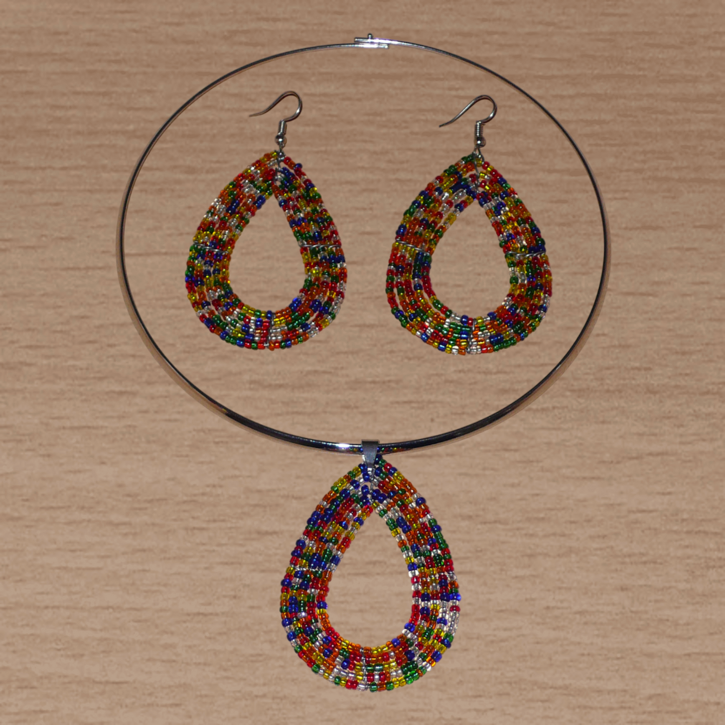Parure contemporaine de bijoux ethniques composée d'un collier ras de cou en laiton agrémenté d'un pendentif en forme de goutte fait d'un mélange de perles de rocaille translucides multicolores, ainsi que d'une paire de boucles d'oreilles assorties au collier.