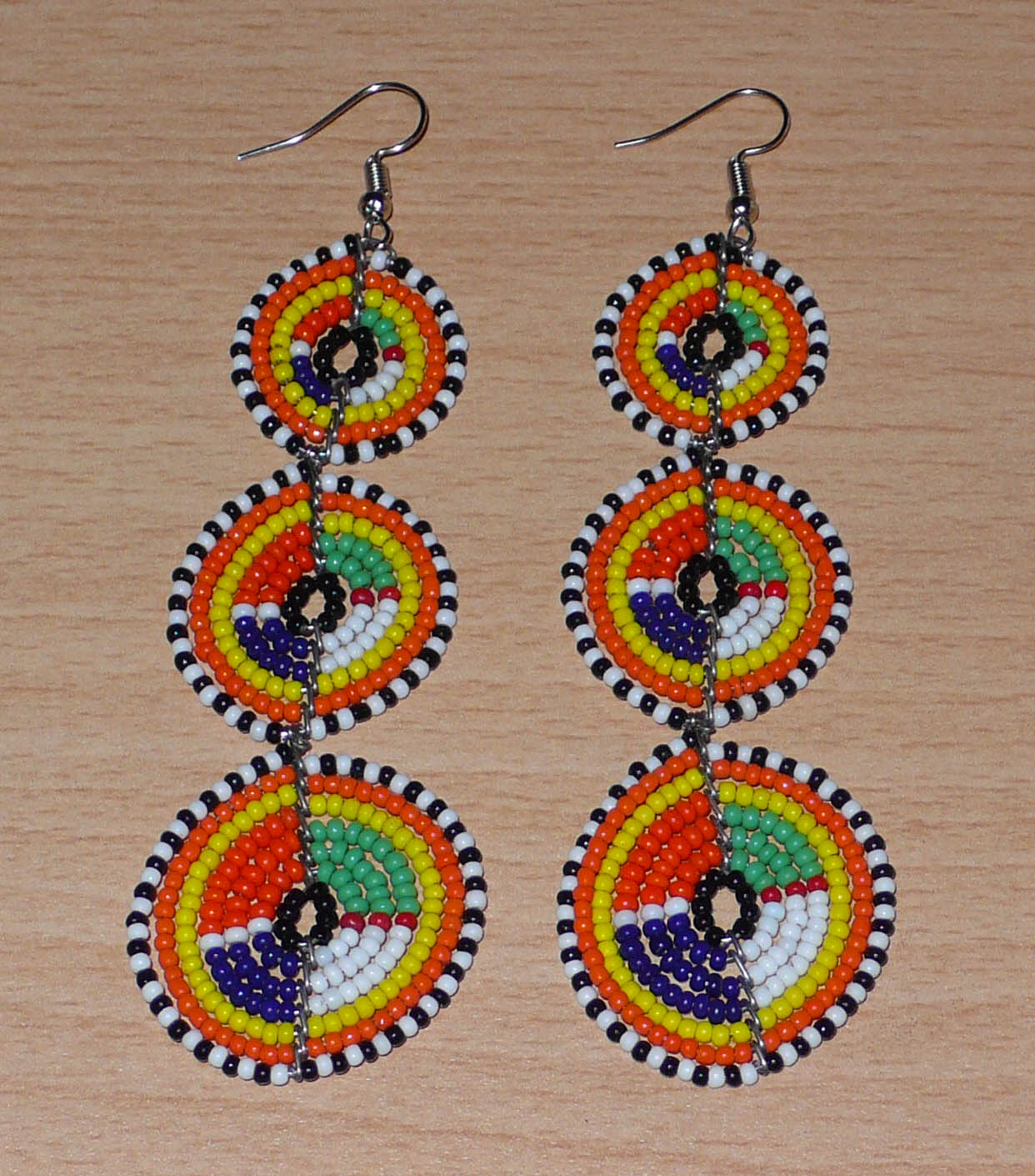 Longues boucles d'oreilles ethniques afro chic composées de perles de rocaille multicolores montées en trois cercles superposés. Elles mesurent 10,5 cm de long et 3 cm de large.