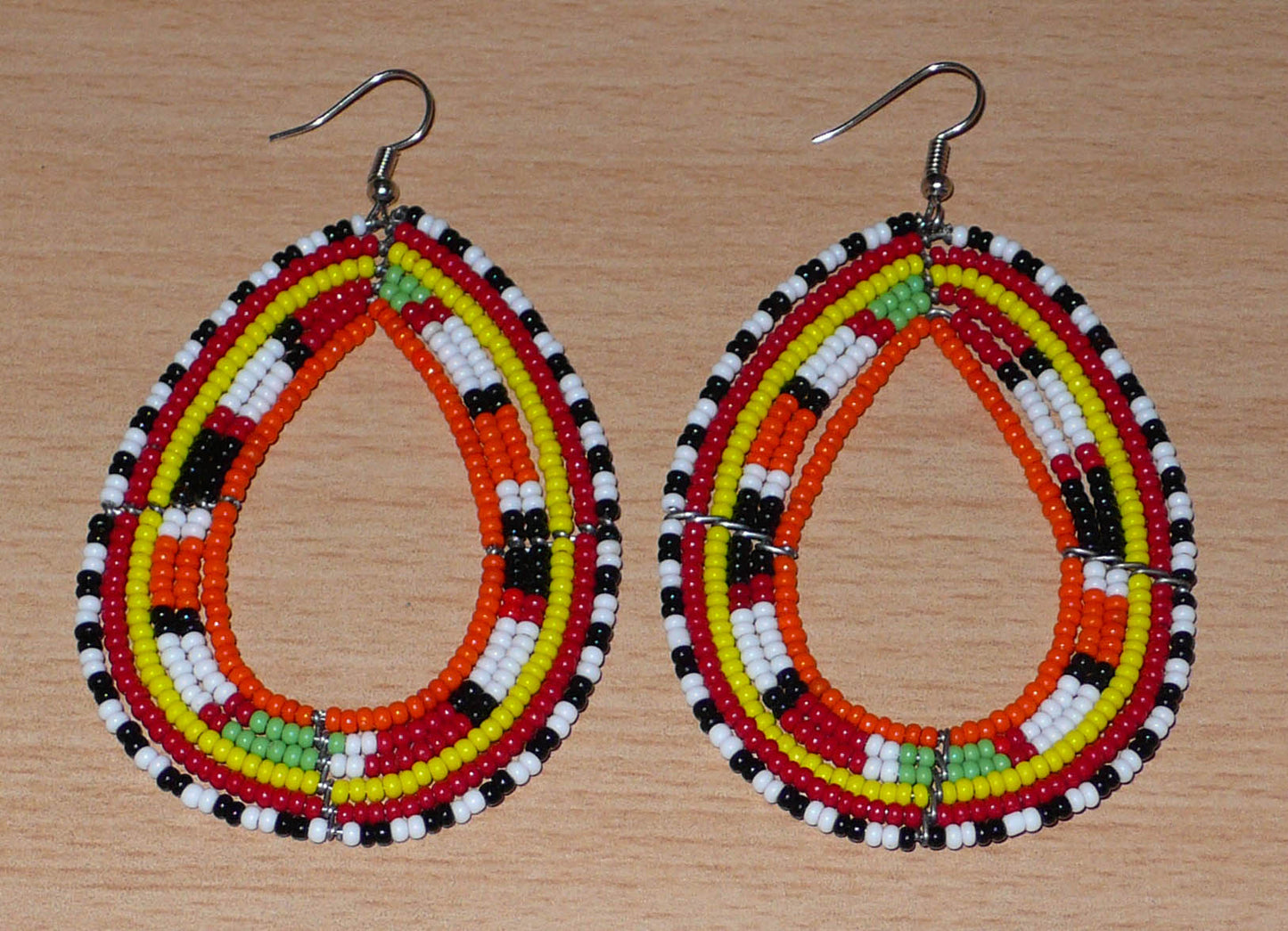 Longues boucles d'oreilles africaines à motifs ethniques Massai faites de perles de rocaille orange et multicolores glissées sur six rangées de fils de fer montés en forme de gouttes. Elles mesurent 8,5 cm de long et 5 cm de large et se portent sur des oreilles percées.