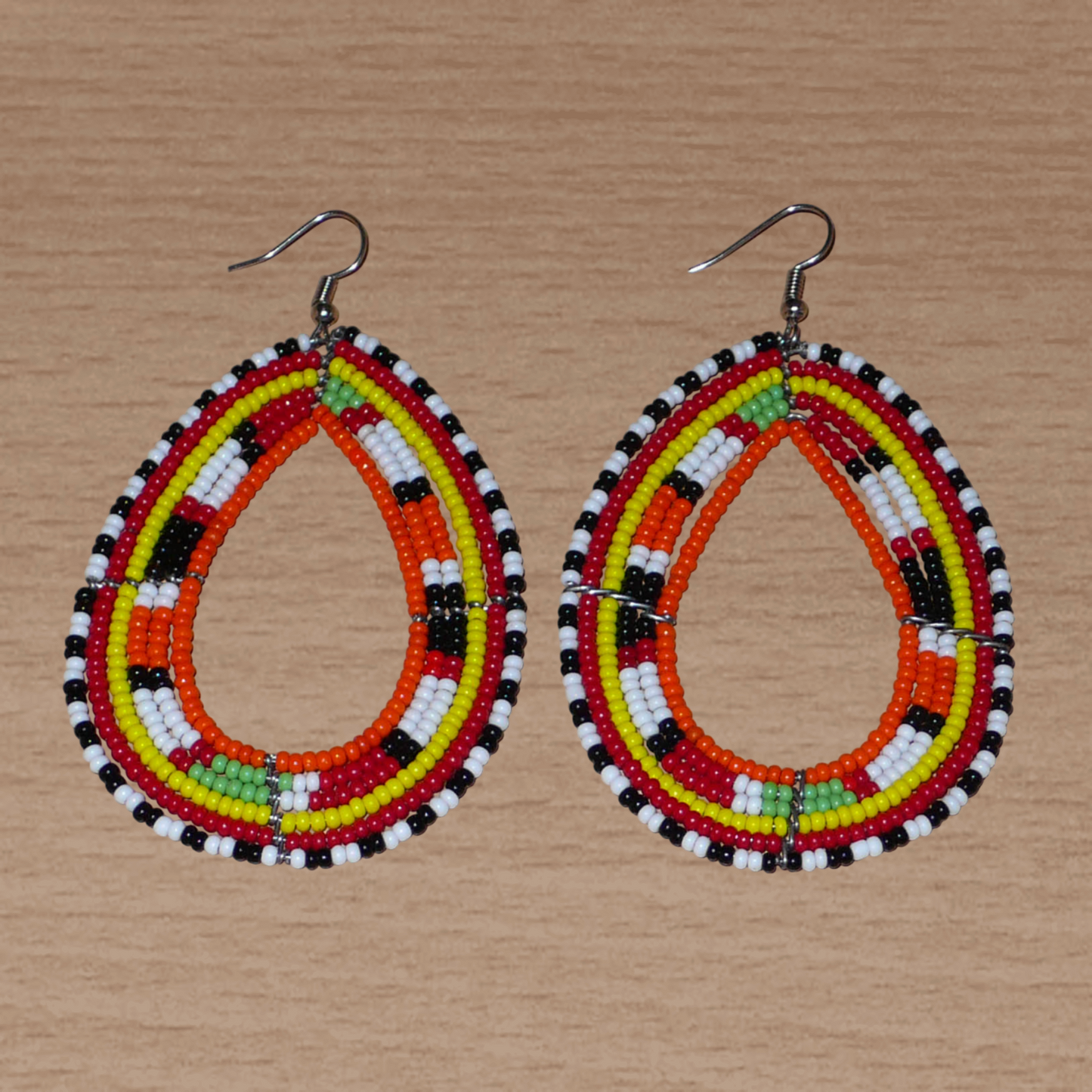 Longues boucles d'oreilles africaines à motifs ethniques Massai faites de perles de rocaille orange et multicolores glissées sur six rangées de fils de fer montés en forme de gouttes. Elles mesurent 8,5 cm de long et 5 cm de large et se portent sur des oreilles percées.
