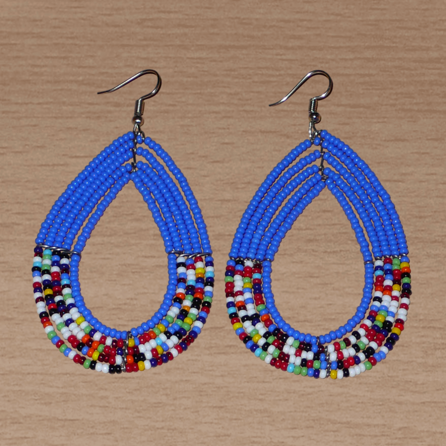 Longues boucles d'oreilles ethniques bleues et multicolores faites de perles de rocaille glissées sur cinq rangées de fils de fer montés en forme de gouttes. Elles mesurent 9 cm de long et 4,5 cm de large, et se portent avec des crochets en acier inoxydable sur des oreilles percées.