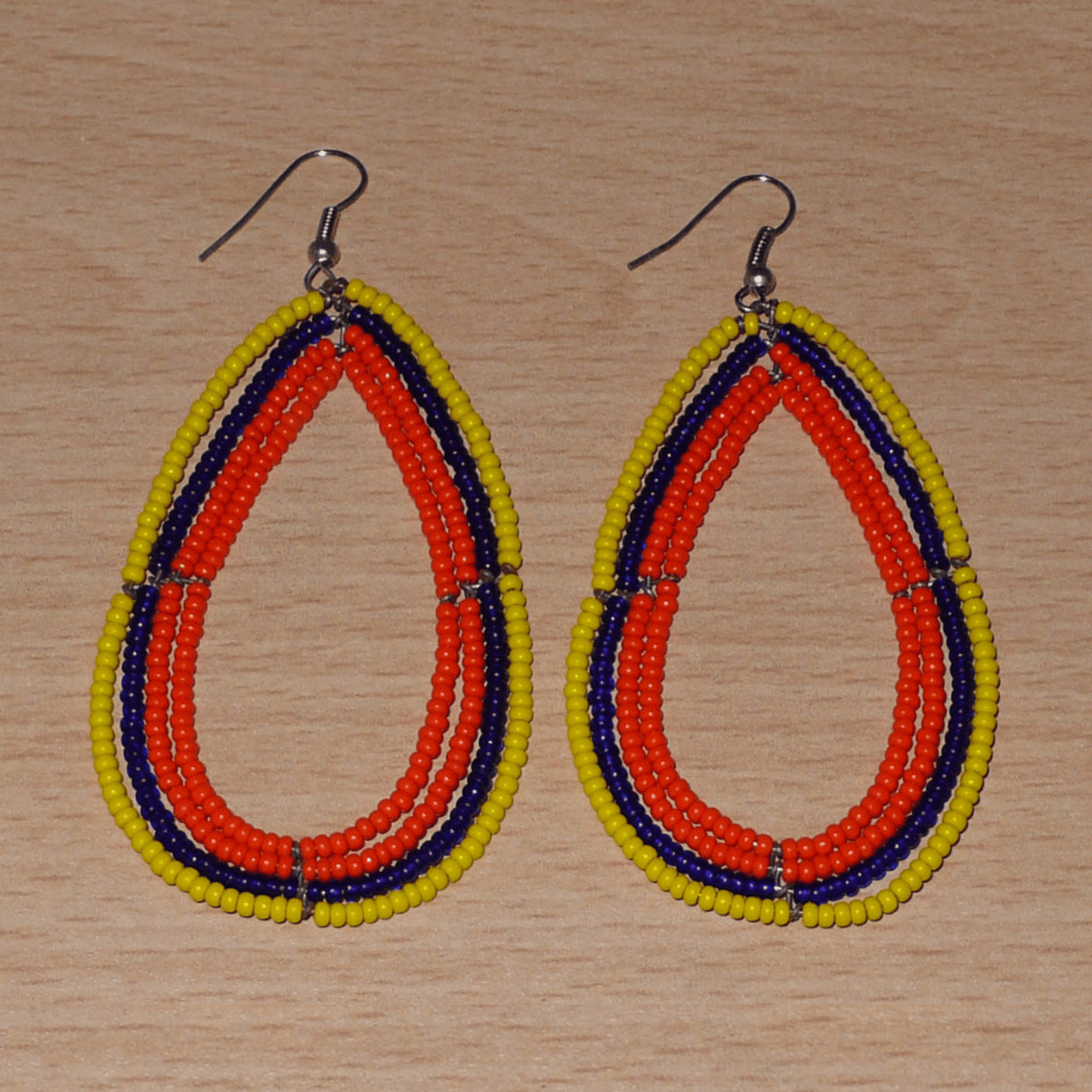 Longues boucles d'oreilles tricolores composées de perles de rocaille orange, jaunes et bleu marine enfilées sur quatre rangées de fils de fer montés en forme de gouttes. Ces boucles d'oreilles "oversized" mesurent 8.5 cm de long et 4.5 cm de large ; elles se portent avec des crochets en acier inoxydable sur des oreilles percées.