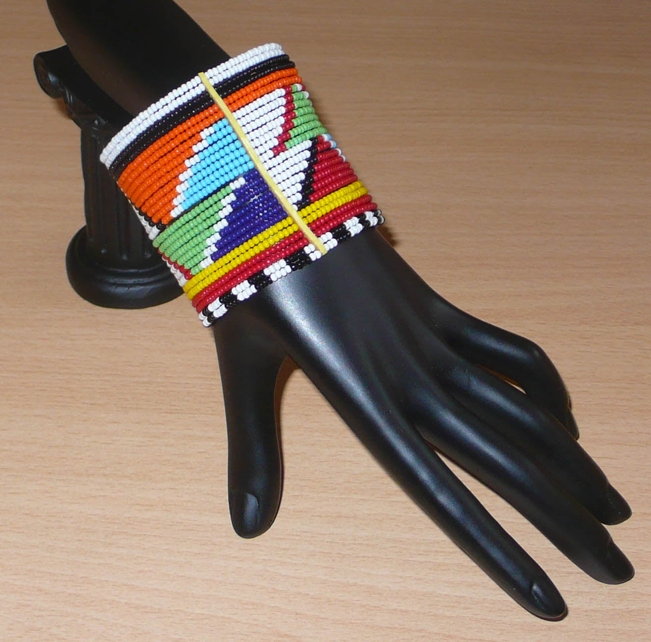 Bracelet africain Massai composé de vingt-six rangées de perles multicolores aux motifs géométriques enfilées sur des fils de fer fixés sur des charnières en plastique. Le bracelet se ferme avec des boutons pressions.