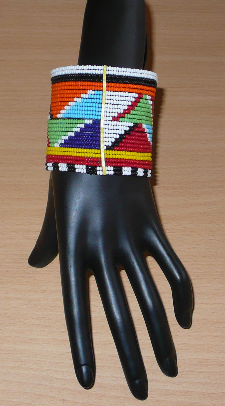Bracelet africain Massai composé de vingt-six rangées de perles multicolores aux motifs géométriques enfilées sur des fils de fer fixés sur des charnières en plastique. Le bracelet se ferme avec des boutons pressions.
