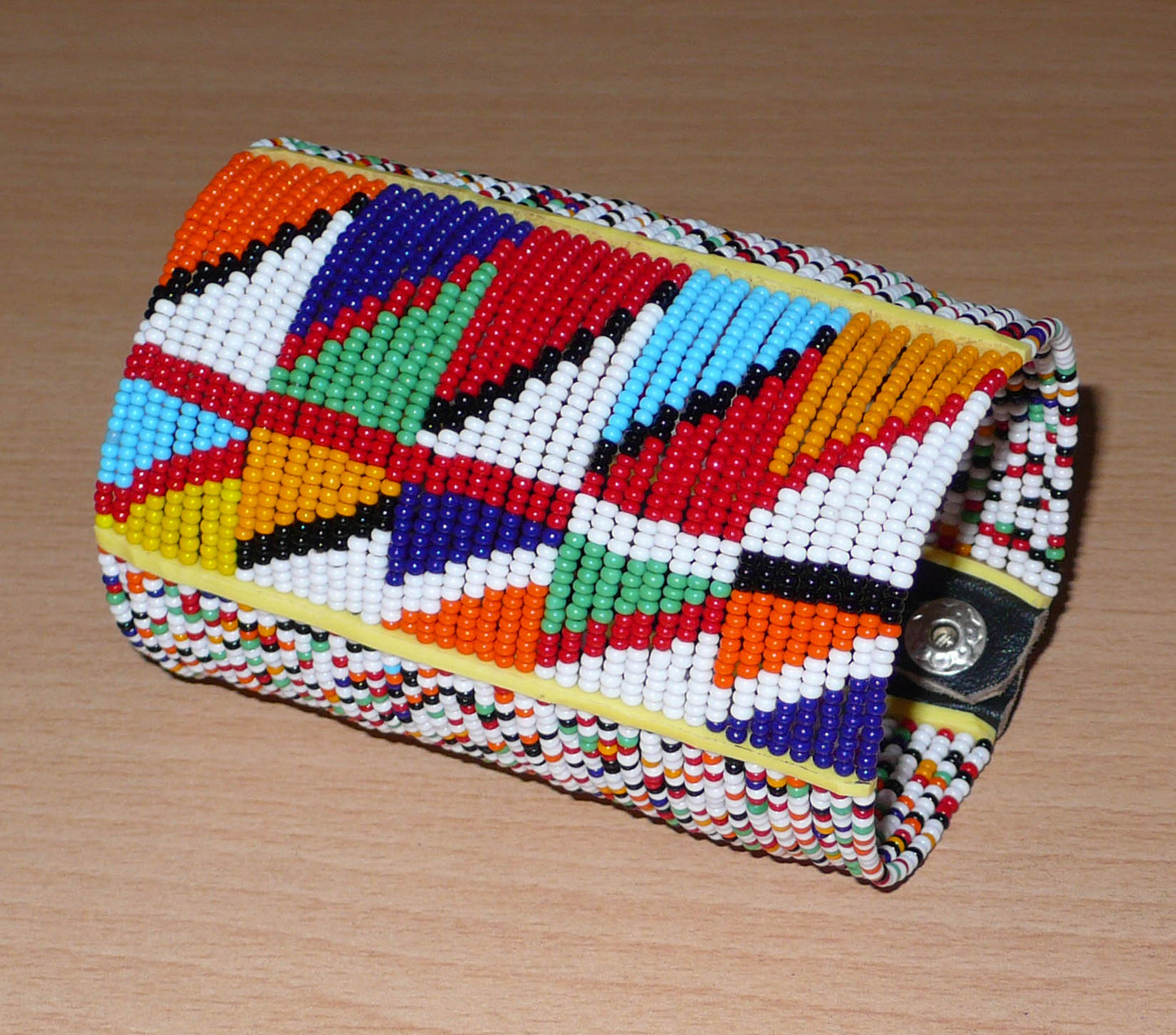 Manchette haute multi-rangs à motifs géométriques ethniques Massai composée de perles de rocaille multicolores ; elle s'attache avec trois boutons pressions.
