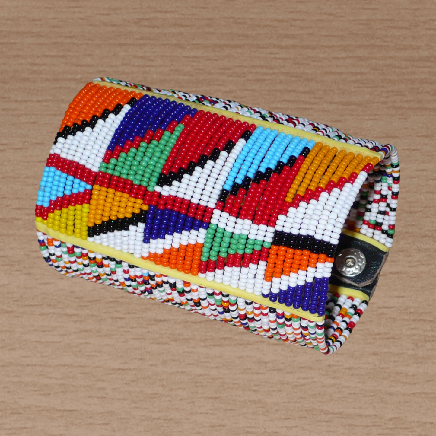 Manchette haute multi-rangs à motifs géométriques ethniques Massai composée de perles de rocaille multicolores ; elle s'attache avec trois boutons pressions.