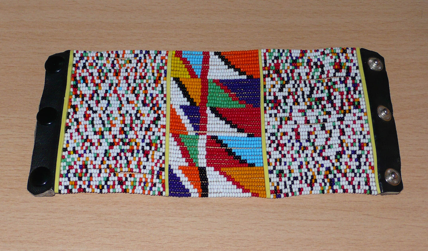 Manchette haute multi-rangs à motifs géométriques ethniques Massai composée de perles de rocaille multicolores ; elle s'attache avec trois boutons pressions.