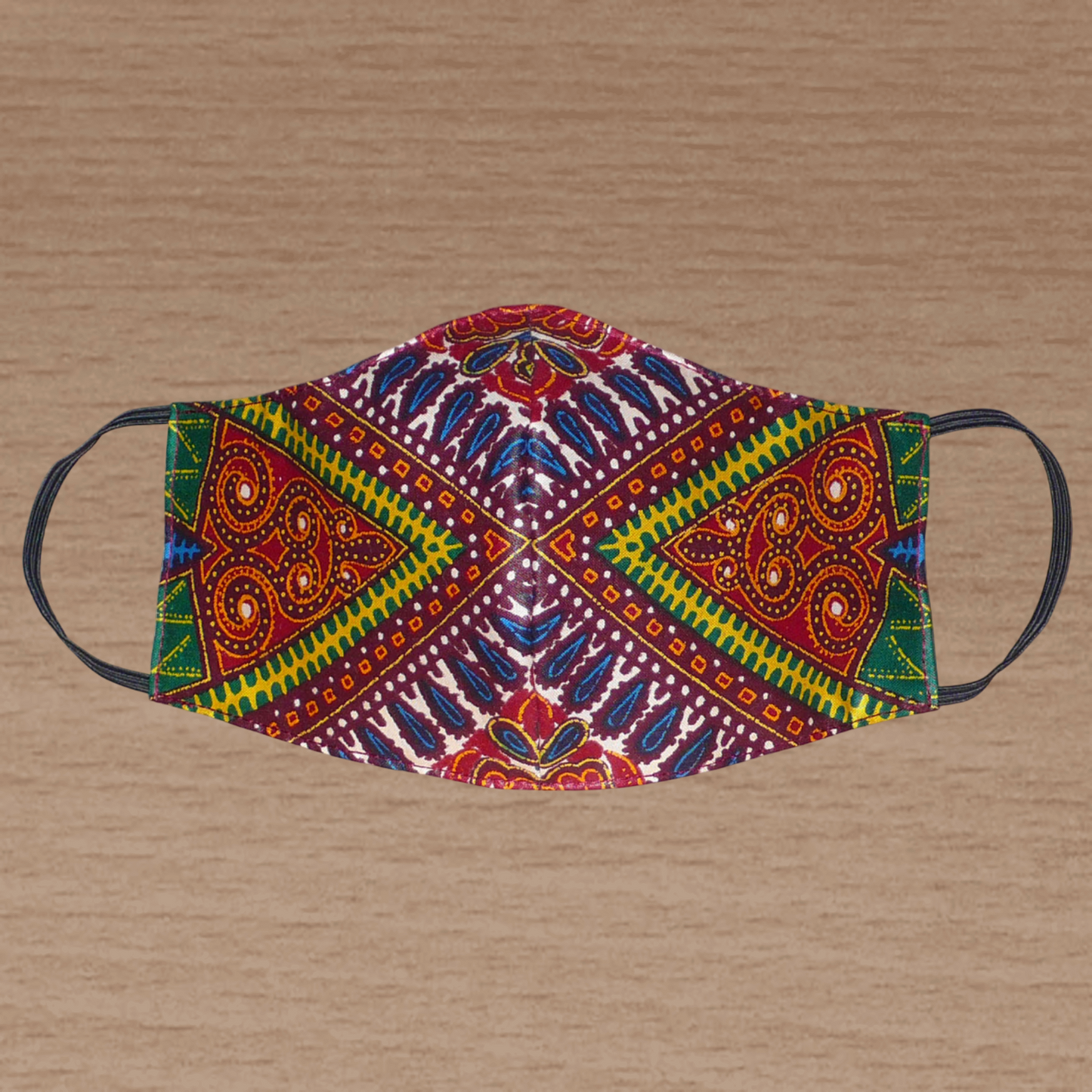 Masque textile ajusté, coupé et cousu dans un tissu africain en coton imprimé de motifs tribaux multicolores ; il se porte avec des élastiques. En vue d'une utilisation éco-responsable, ce masque est lavable et réutilisable. Ce masque à l'allure ethnique chic mesure 21 cm de long, et 40 cm en comptant les élastiques ; il a une hauteur de 12 cm (du haut du nez jusqu'au menton) et une largeur sur les côtés de 7 cm.