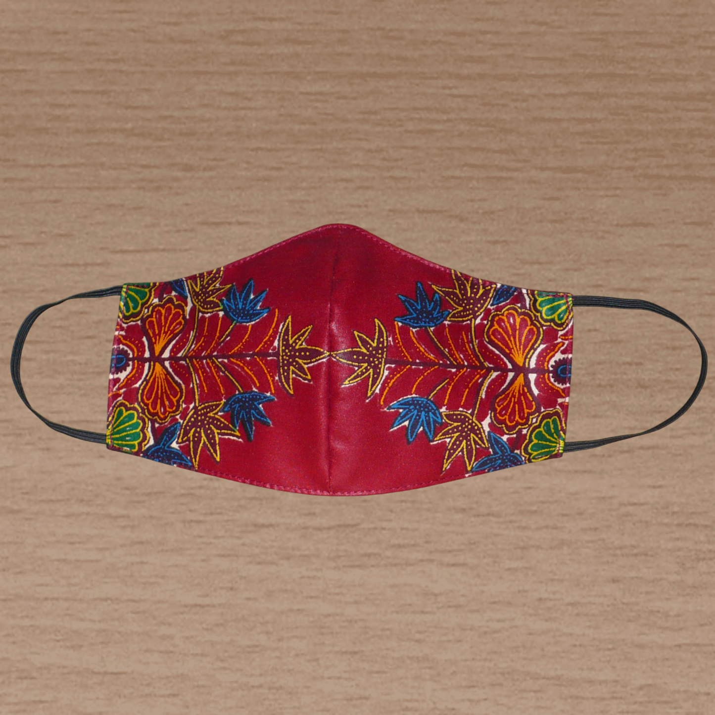 Masque facial textile coupé et cousu dans un tissu en coton à motifs africains bordeaux et multicolores ; il se porte avec des élastiques. Dans une démarche éco-responsable, il est lavable et réutilisable. Ce masque à l'allure ethnique mesure 21 cm de long, et 40 cm en comptant les élastiques ; il a une hauteur de 12 cm (du haut du nez jusqu'au menton) et une largeur sur les côtés de 7 cm.