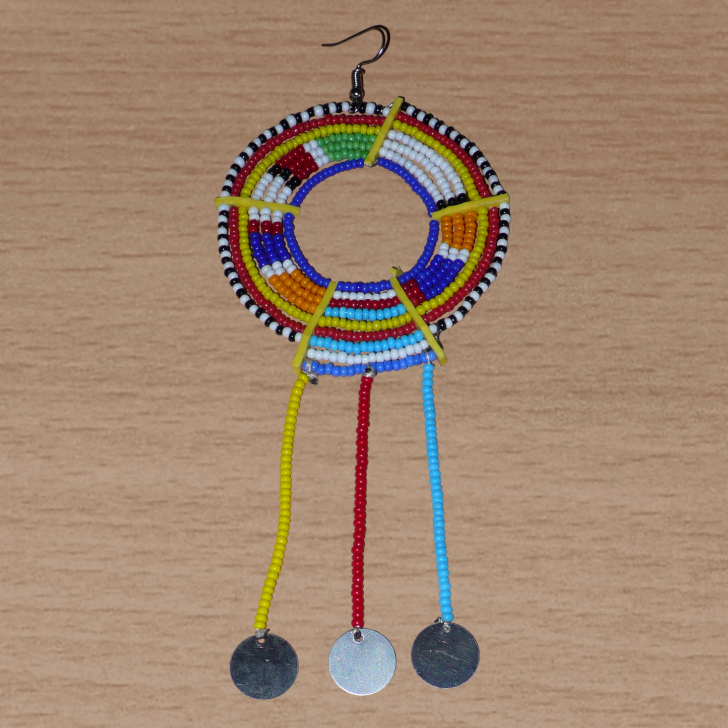 Mono boucle d'oreille africaine Massai à porter sur une seule oreille pour créer un effet d'asymétrie visuelle : elle se compose de perles de rocaille bleues et multicolores enfilées sur des fils de fer montés en cercles fixés sur des charnières en plastique recyclé jaune ; il se prolonge de franges perlées ornées de disques en métal. Surdimensionnée, cette mono boucle d'oreille à l'allure exotique mesure 15 cm de long.