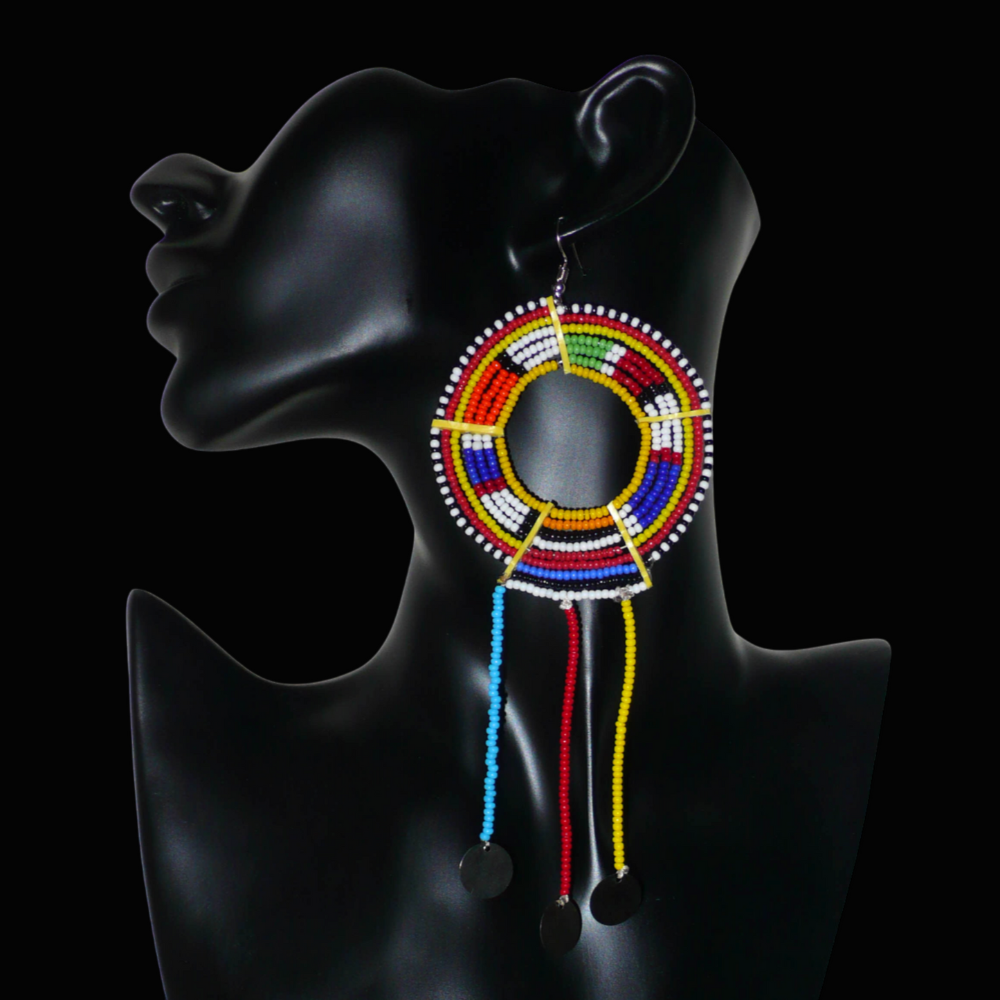 Mono boucle d'oreille à franges fabriquée au Kenya dans la tradition ethnique Massai. À porter sur une seule oreille pour un effet visuel asymétrique, ce bijou se compose de perles de rocaille multicolores glissées sur des fils de fer montés en cercles fixés sur des charnières en plastique recyclé jaune ; il se prolonge de franges perlées ornées de disques en métal. Surdimensionnée, elle mesure 16.5 cm de long et 6.5 cm de large, et se porte sur une oreille percée.