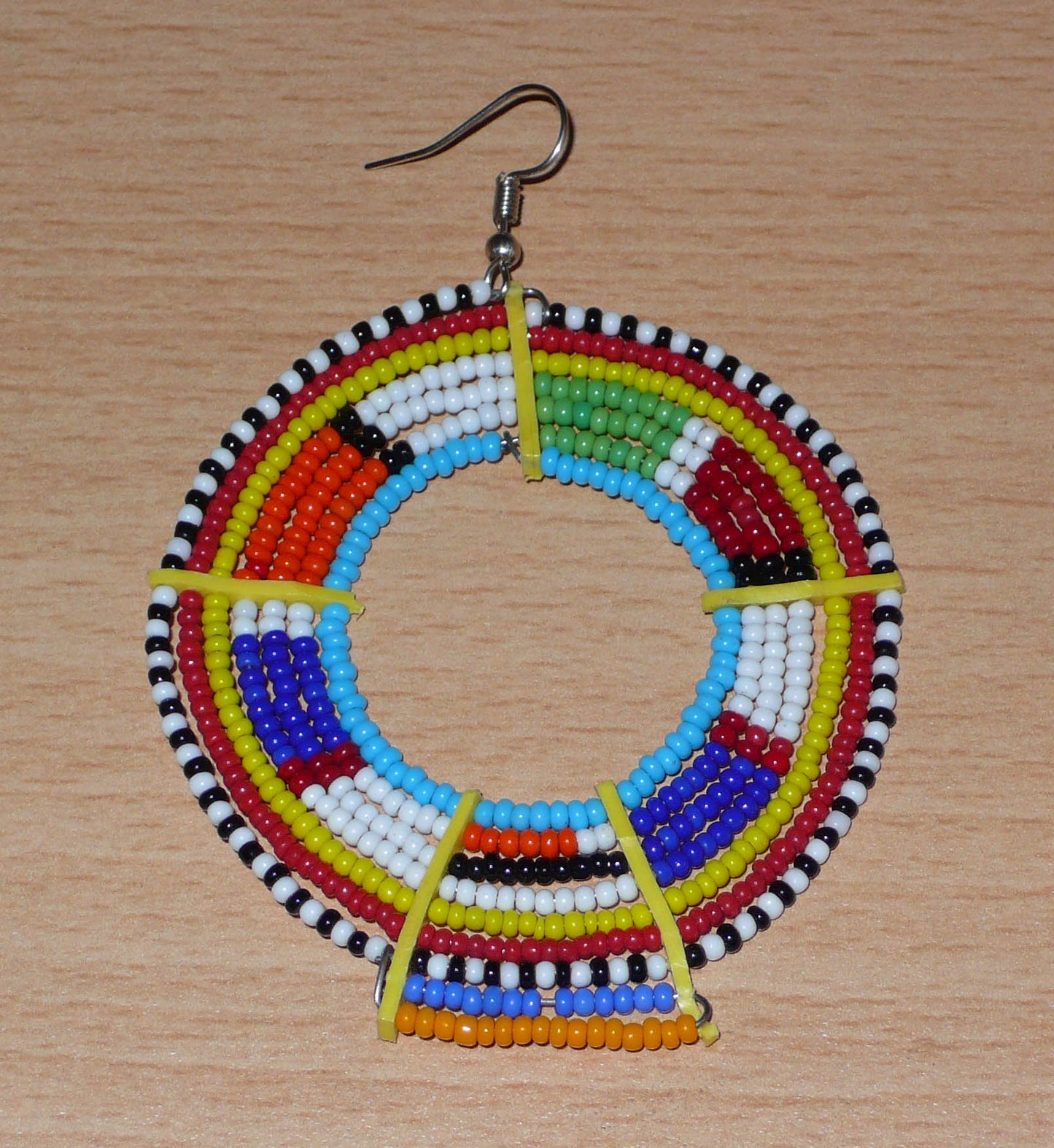 Ajoutez une touche ultra colorée à votre look avec cette mono boucle africaine Massai, à porter sur une seule oreille pour un effet visuel asymétrique ! De fabrication traditionnelle kenyane, ce bijou artisanal se compose de perles de rocaille bleues et multicolores glissées sur des fils de fer montés en cercles et fixés sur des charnières en plastique recyclé jaune. Surdimensionnée, elle mesure 8.5 cm de long et 6 cm de large, et se porte avec un crochet sur une oreille percée.