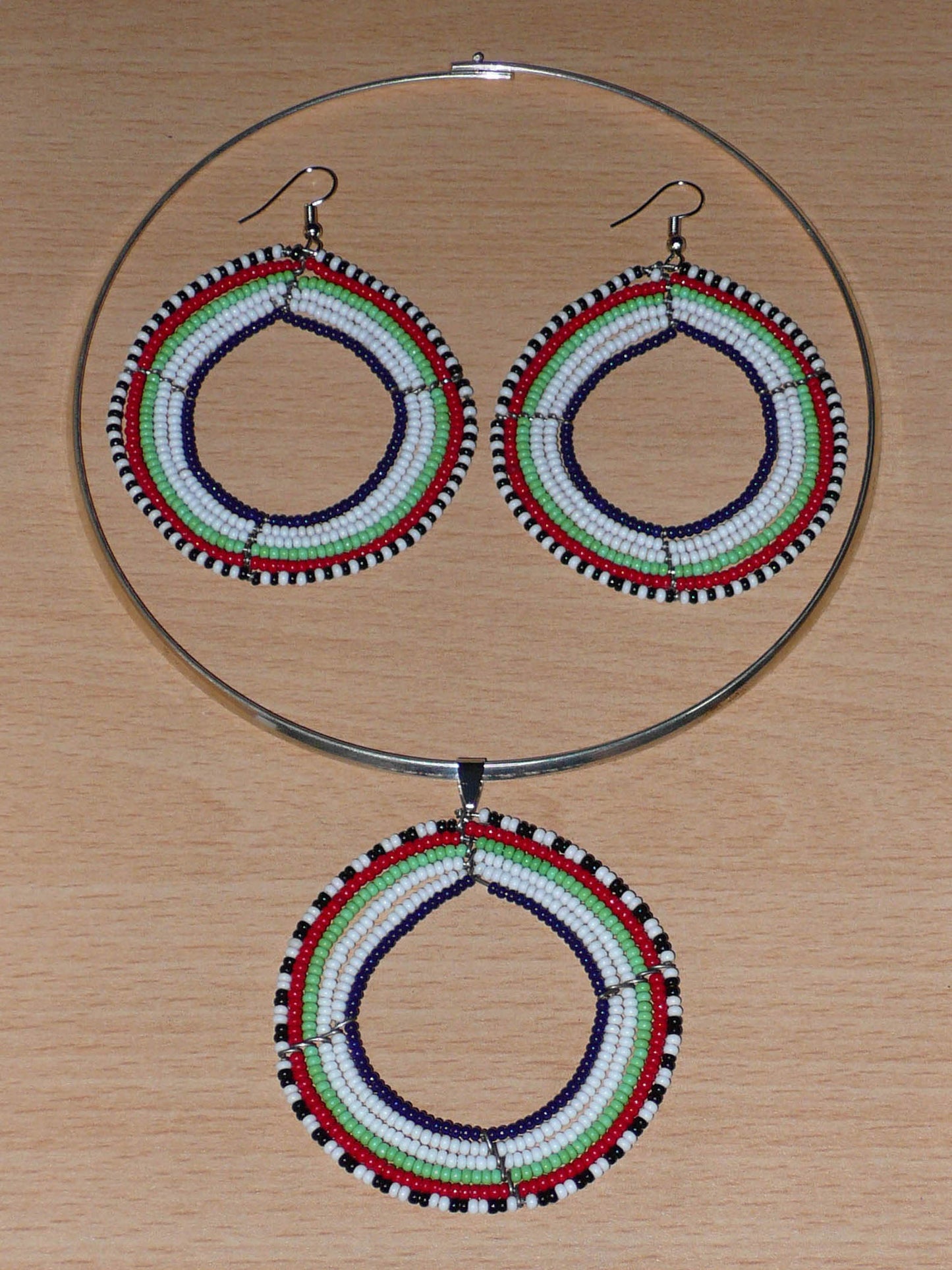Parure de bijoux africains Massai au style hippie chic des années 70 composée d'un collier ras de cou en laiton orné d'un large médaillon fait de perles de rocaille blanches, vertes, rouges, noires et bleu marine, et d'une paire de boucles d'oreilles rondes assorties.