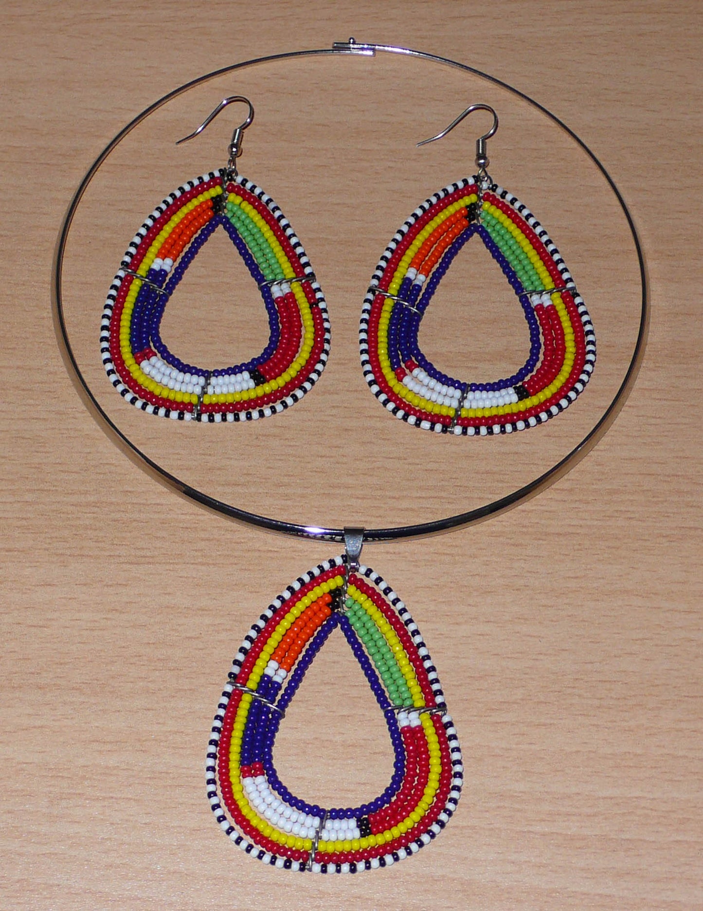 Parure contemporaine de bijoux africains mêlant tradition africaine et modernité. Cet ensemble se compose d'un collier ras-de-cou en laiton agrémenté d'un pendentif Massai en forme de triangle aux bords arrondis en perles de rocaille bleu foncé et multicolores, et d'une paire de boucles d'oreilles ethniques assorties.