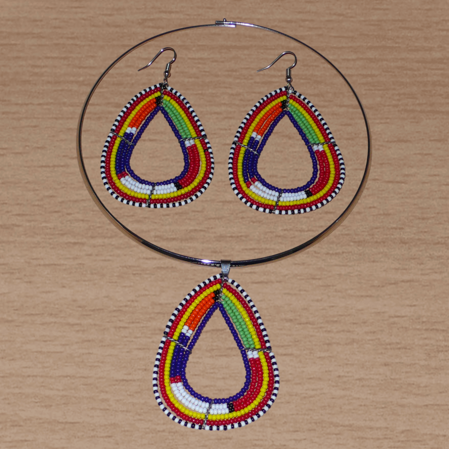 Parure contemporaine de bijoux africains mêlant tradition africaine et modernité. Cet ensemble se compose d'un collier ras-de-cou en laiton agrémenté d'un pendentif Massai en forme de triangle aux bords arrondis en perles de rocaille bleu foncé et multicolores, et d'une paire de boucles d'oreilles ethniques assorties.