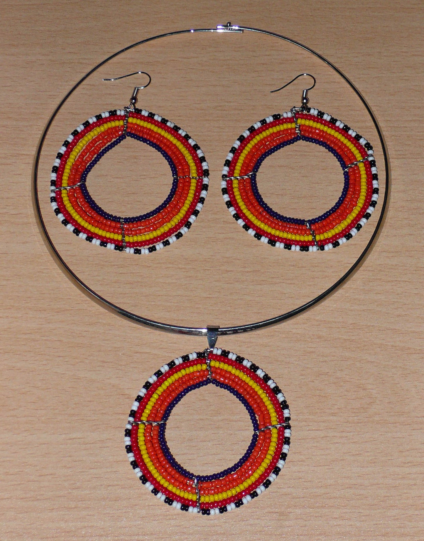 Parure de bijoux ethniques principalement orange comprenant un collier ras de cou en laiton orné d'un large médaillon fait de perles de rocaille, et une paire de boucles d'oreilles assorties.