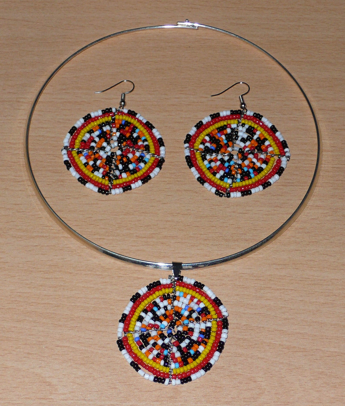 Parure de bijoux ethniques se composant d'un collier ras de cou en laiton orné d'un médaillon fait d'un mélange de perles de rocaille, et d'une paire de boucles d'oreilles rondes assorties.