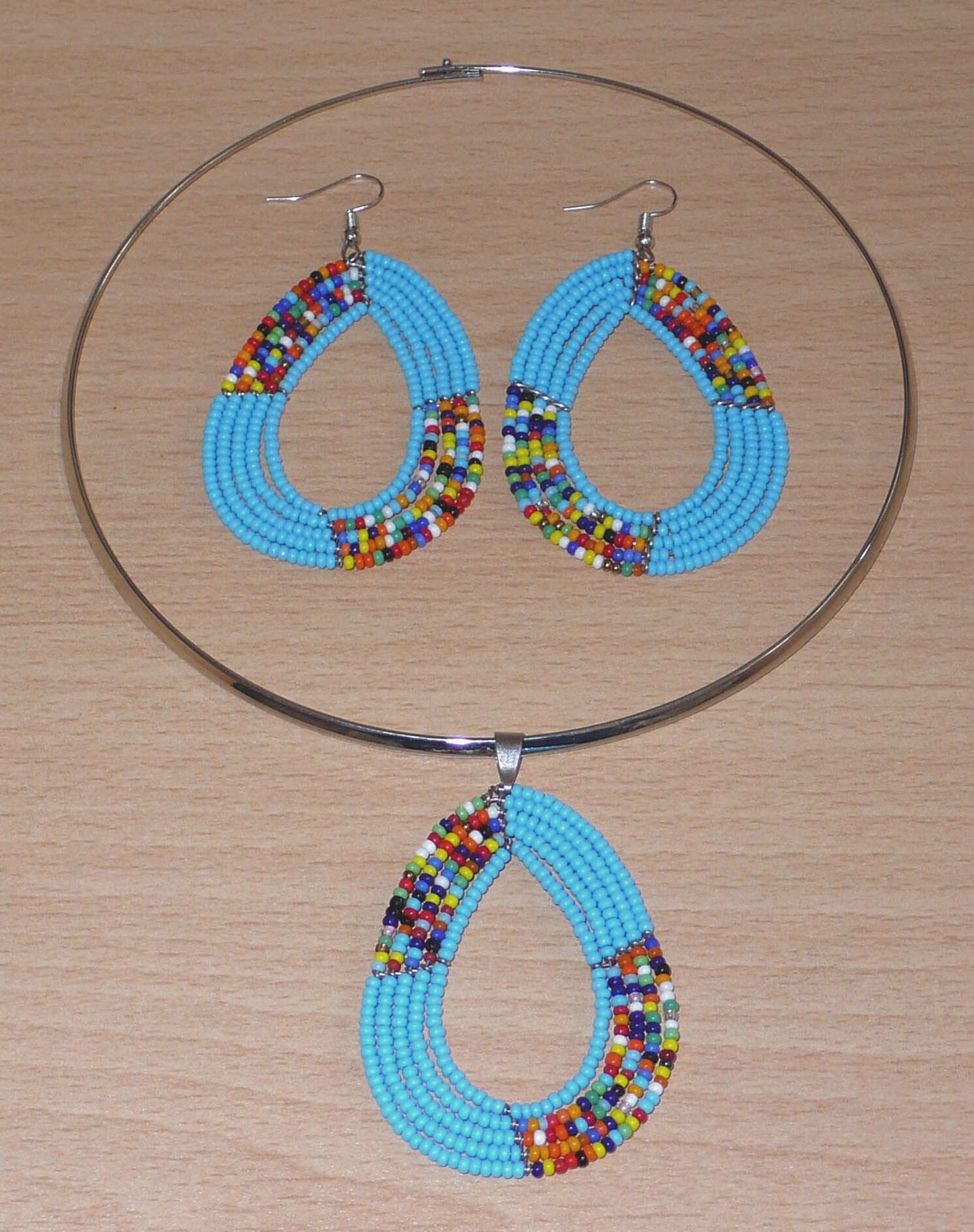 Parure de bijoux ethniques bleus aux accents bohème chic composée d'un collier ras de cou orné d'un pendentif fait de perles de rocaille bleu ciel et multicolores montées en forme de goutte, et d'une paire de boucles d'oreilles assorties.
