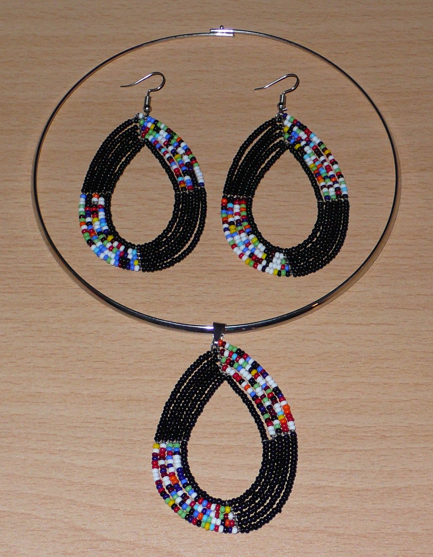 Parure de bijoux ethniques noirs et multicolores composée d'un collier ras de cou en laiton orné d'un long pendentif en forme de goutte fait de perles de rocaille, et d'une paire de boucles d'oreilles assorties.