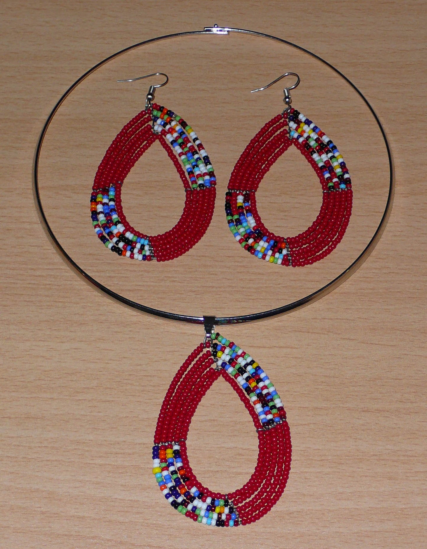Parure contemporaine de bijoux ethniques rouges et multicolores se composant d'un collier ras de cou en laiton agrémenté d'un pendentif perlé en forme de goutte, et d'une paire de boucles d'oreilles assorties.