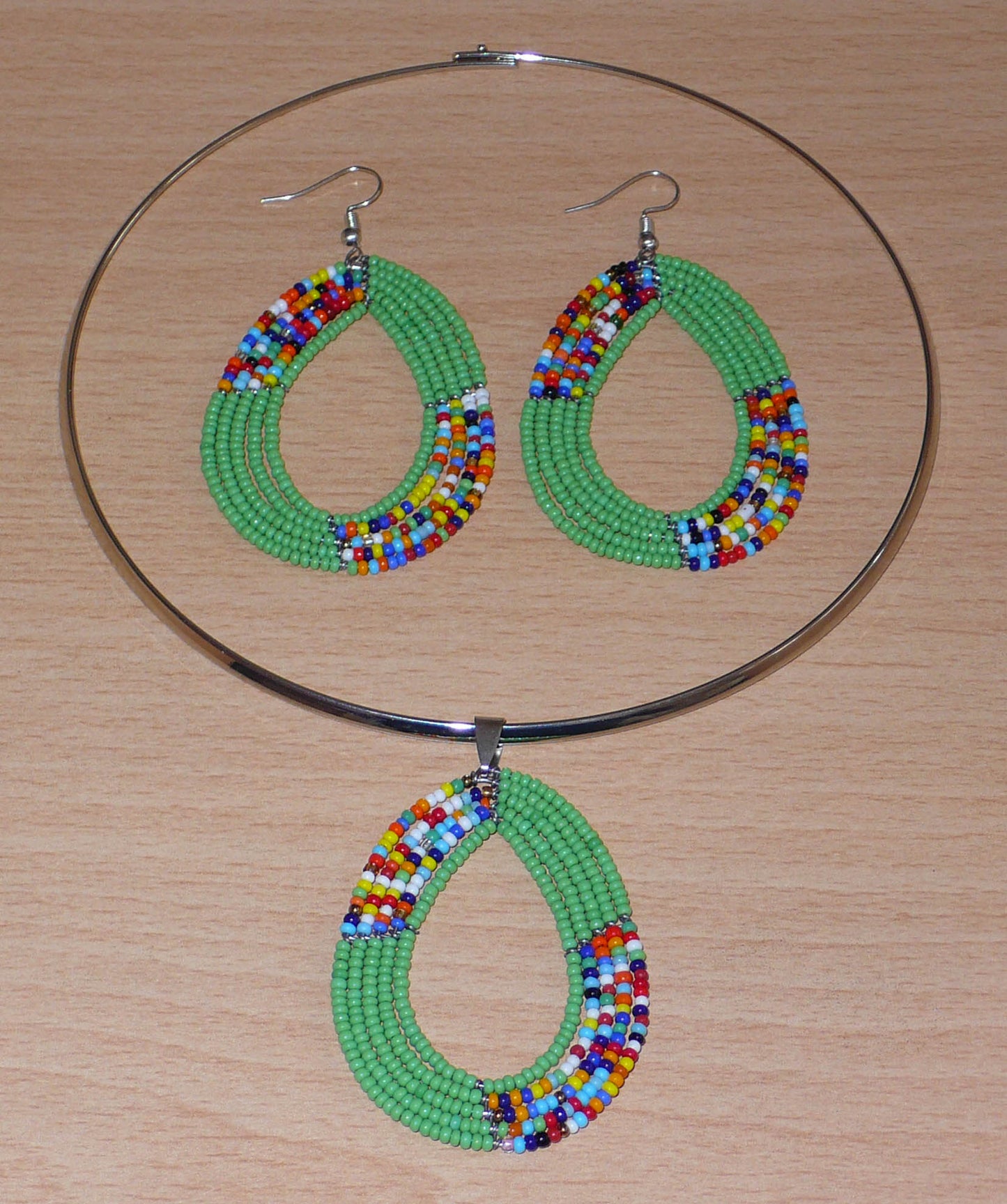 Parure contemporaine de bijoux ethniques verts aux accents bohème composée d'un collier ras de cou en laiton agrémenté d'un pendentif en perles de rocaille vertes et multicolores glissées sur cinq rangées de fils de fer montés en forme de goutte, et d'une paire de boucles d'oreilles assorties.