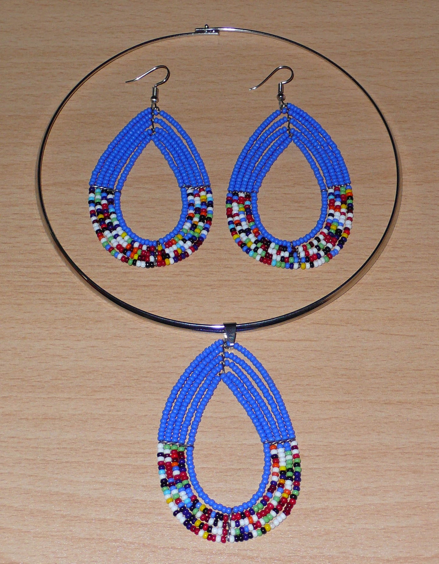 Parure de bijoux ethniques bleus composée d'un ras de cou en laiton orné d'un long pendentif fait de perles de rocaille bleues et multicolores montées en forme de goutte, et d'une paire de longues boucles d'oreilles assorties au collier.