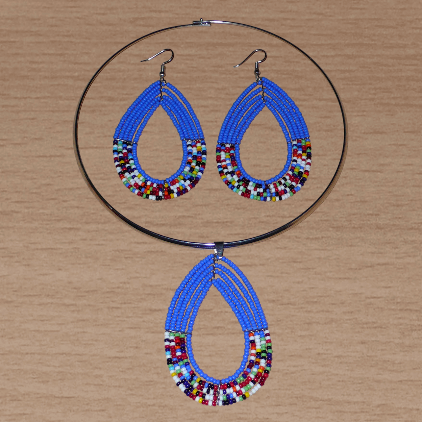 Parure de bijoux ethniques bleus composée d'un ras de cou en laiton orné d'un long pendentif fait de perles de rocaille bleues et multicolores montées en forme de goutte, et d'une paire de longues boucles d'oreilles assorties au collier.